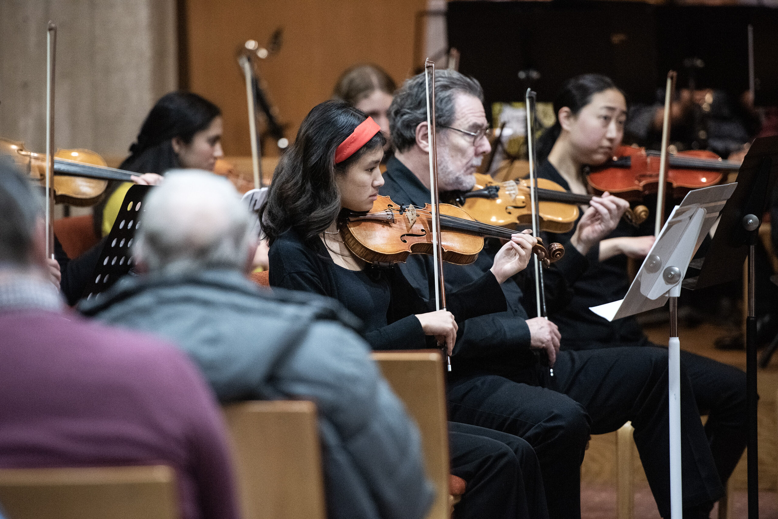 A line of violinists play music as an audience watches from church pews.