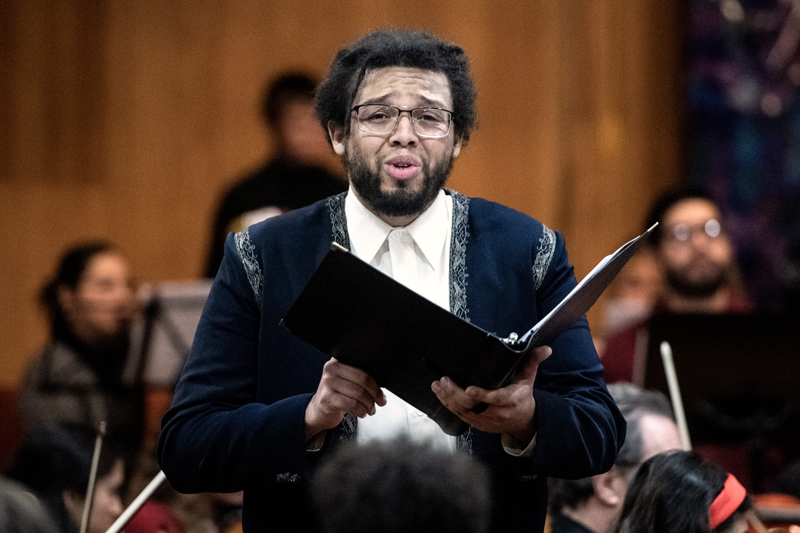 A singer holds a book of music and looks out at the audience while singing.