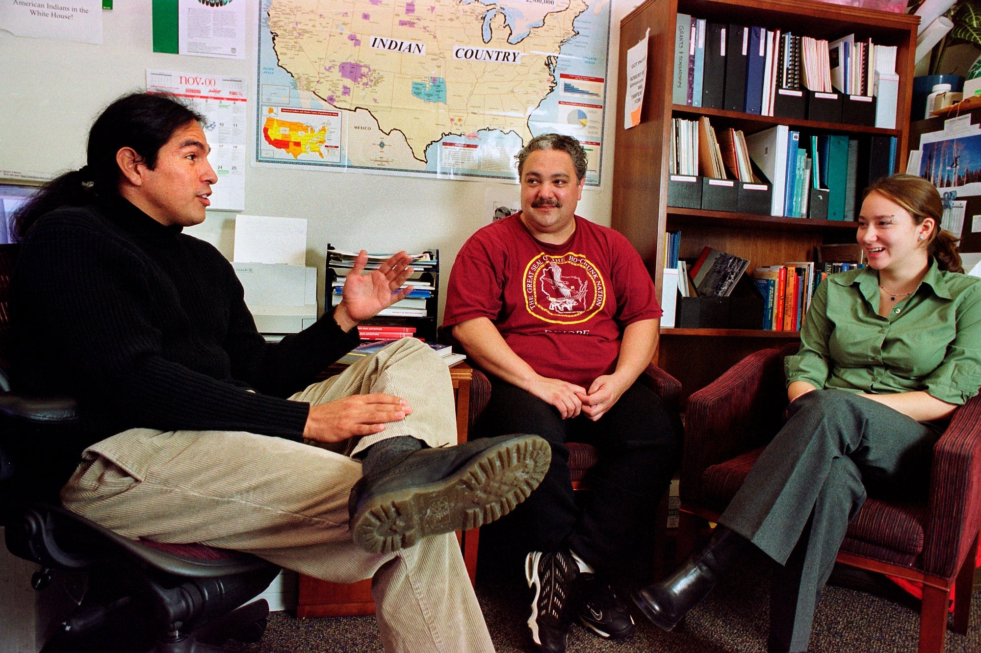 Aaron Bird Bear sits next to two students in his office