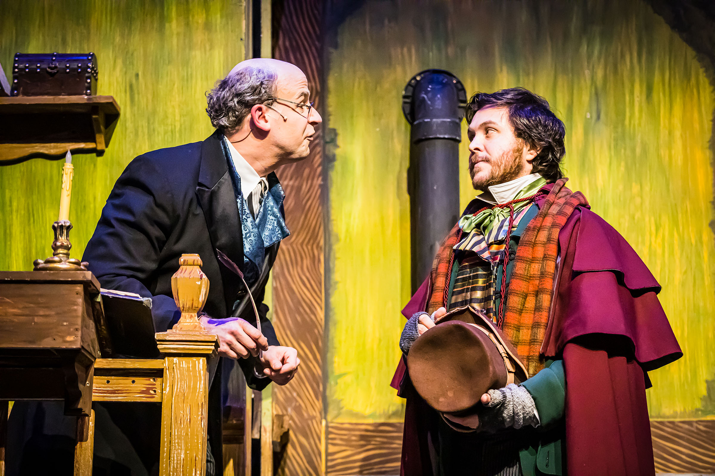 A man playing Ebenezer Scrooge leans in and talks to another character during a performance