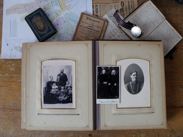 An old photo book lies on a table. It's open and there are two old pictures of women seated on chairs.