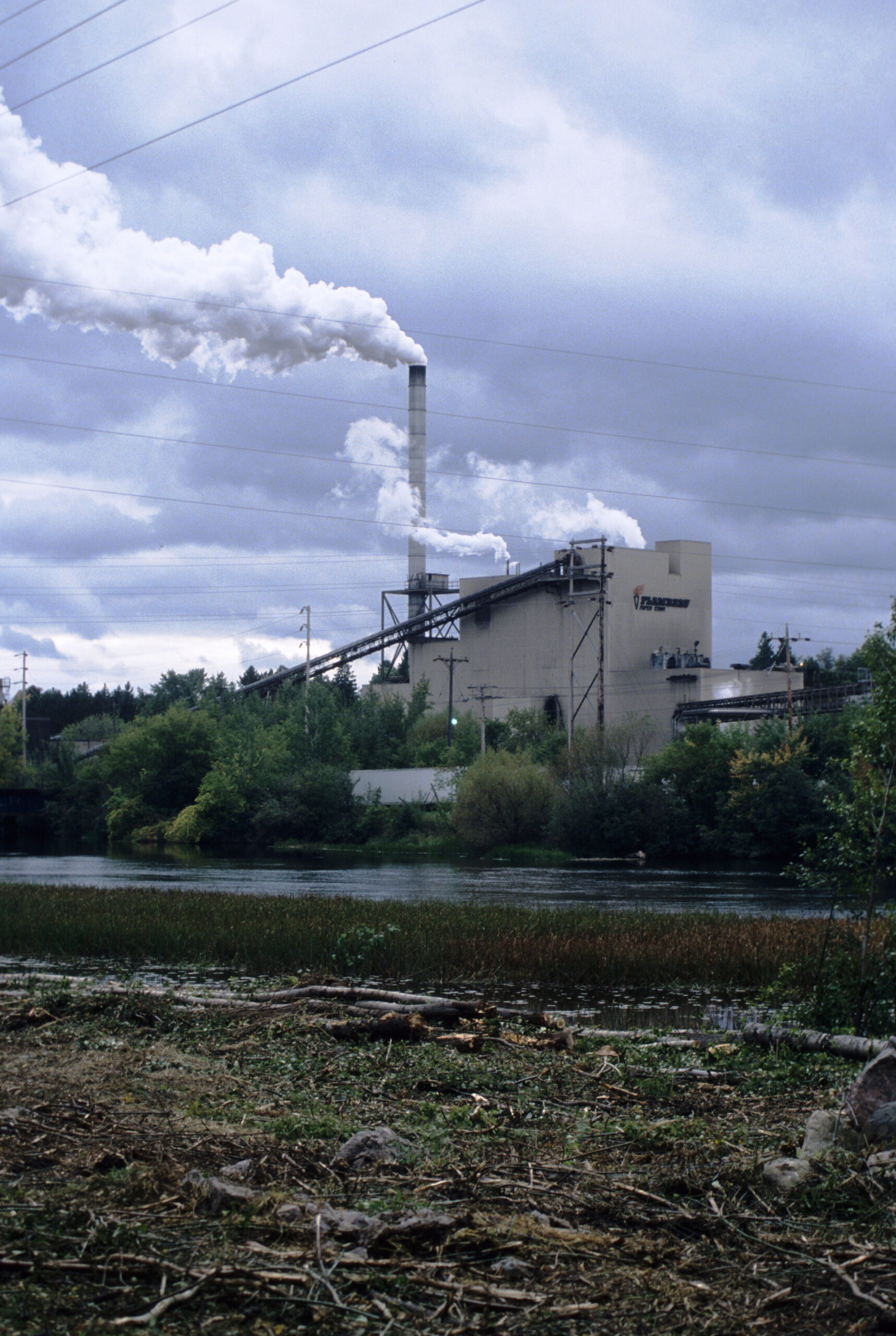 A paper mill with factory smoke coming out the top sits next to the Flambeau River