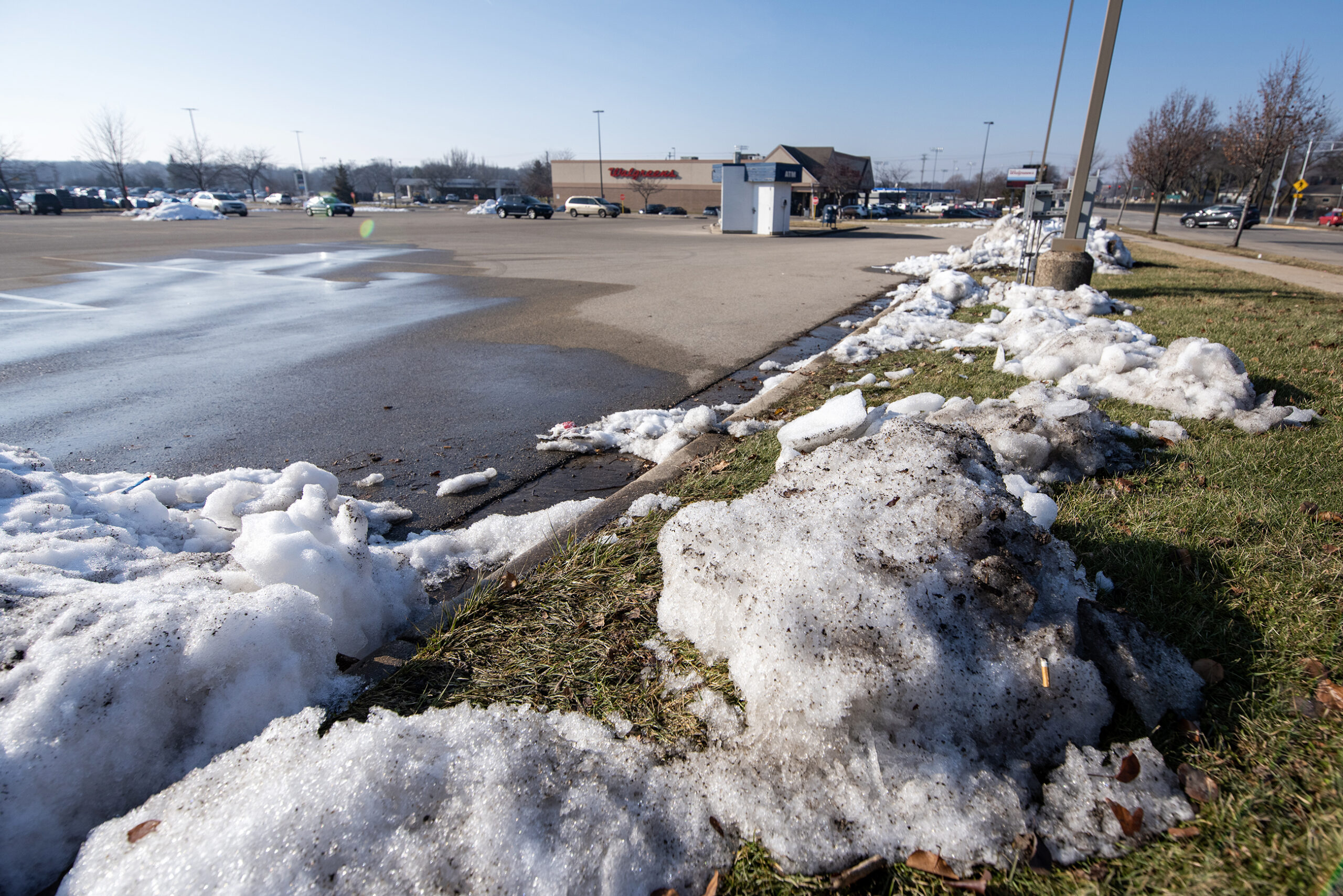 Piles of snow mixed with dirt melt in a parking lot on a sunny day.