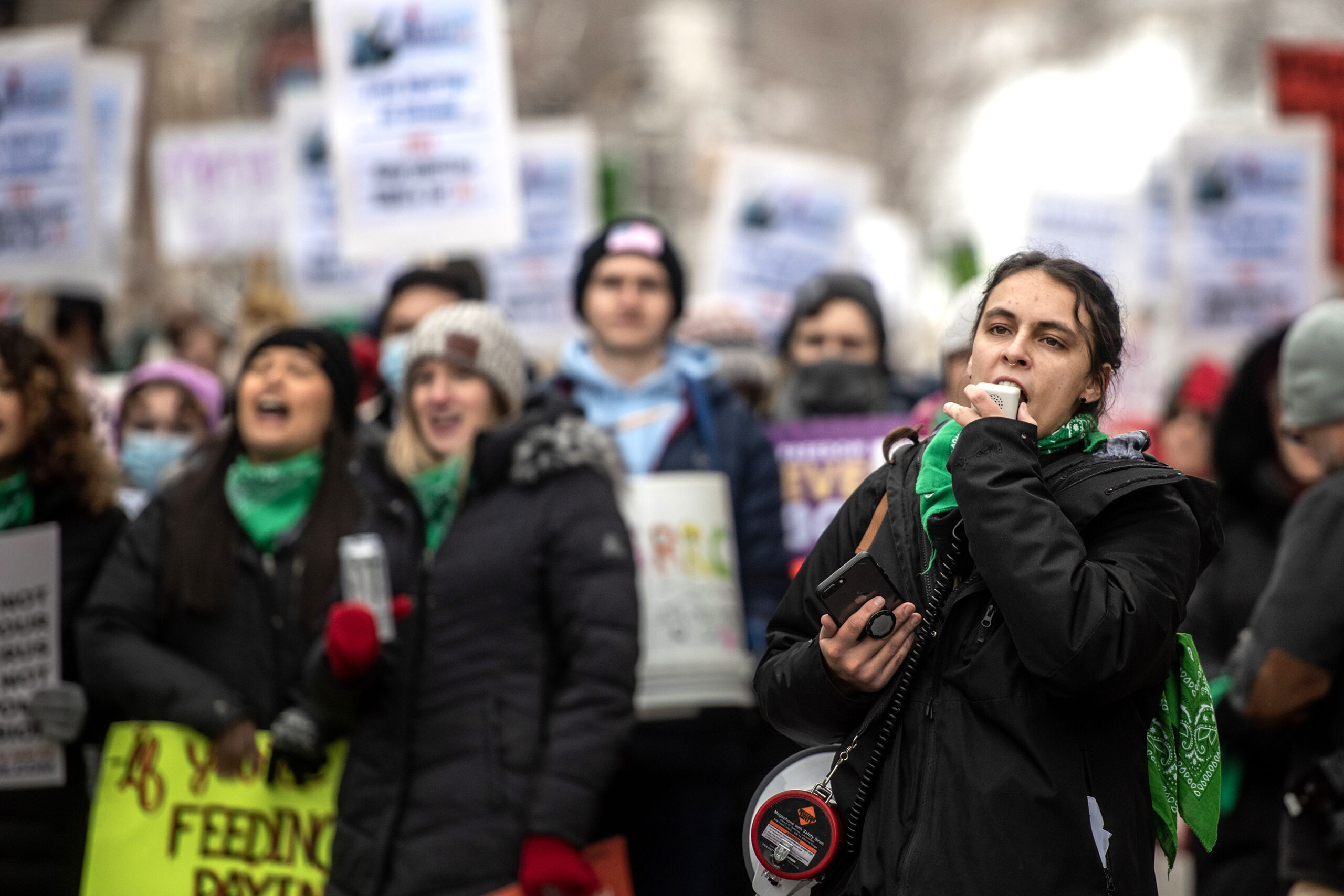 A protest leader shouts into a megaphone as protesters stand behind her.