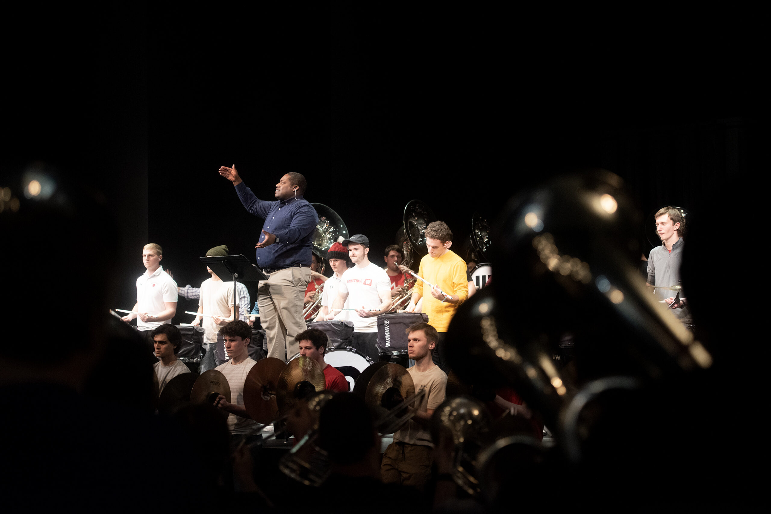 A director waves his arms as students play instruments in a theater.