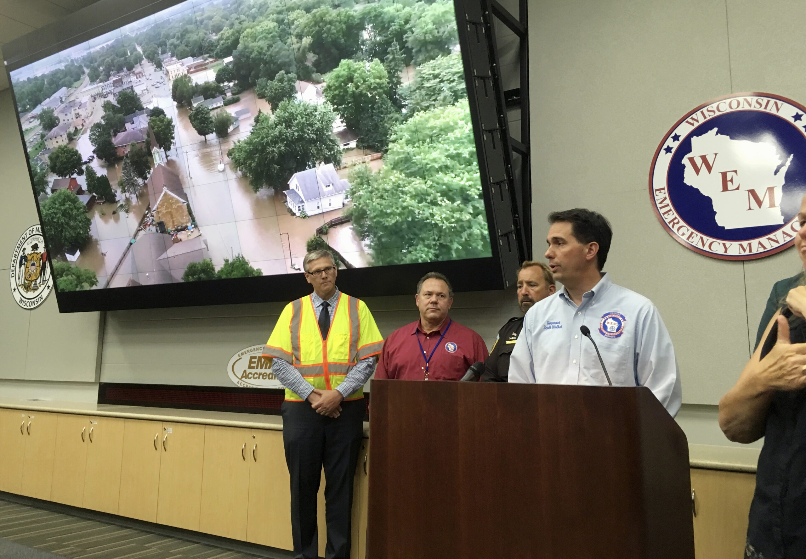 Gov. Scott Walker talking in front of arial photo of flooded neighborhood