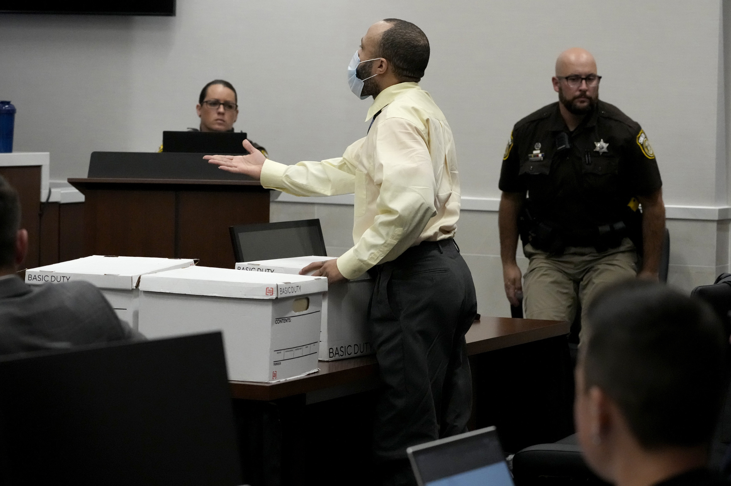 Darrell Brooks stands at his table in court with white boxes in front of him on the table