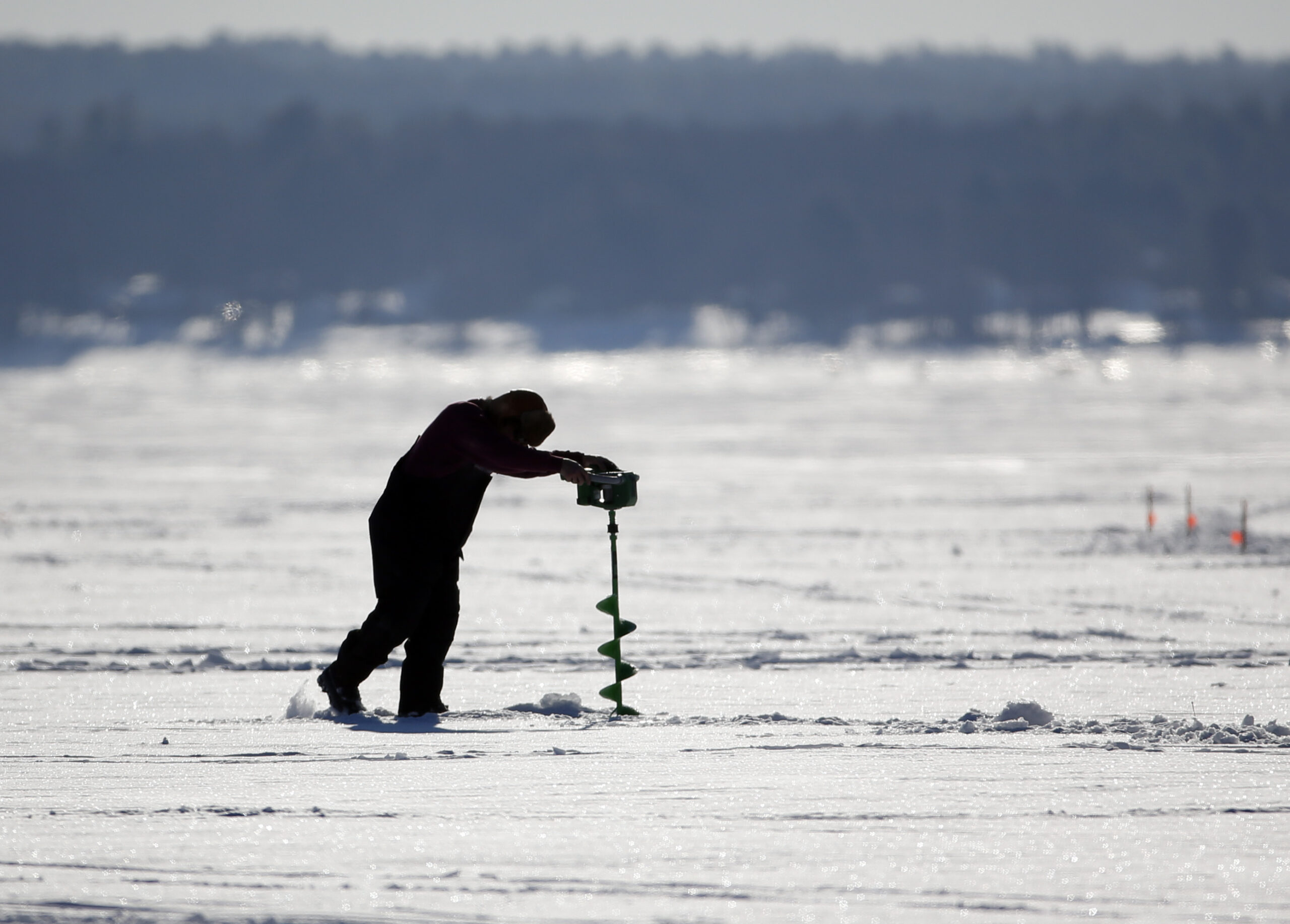 An ice fisher drills a hole on a frozen lake.