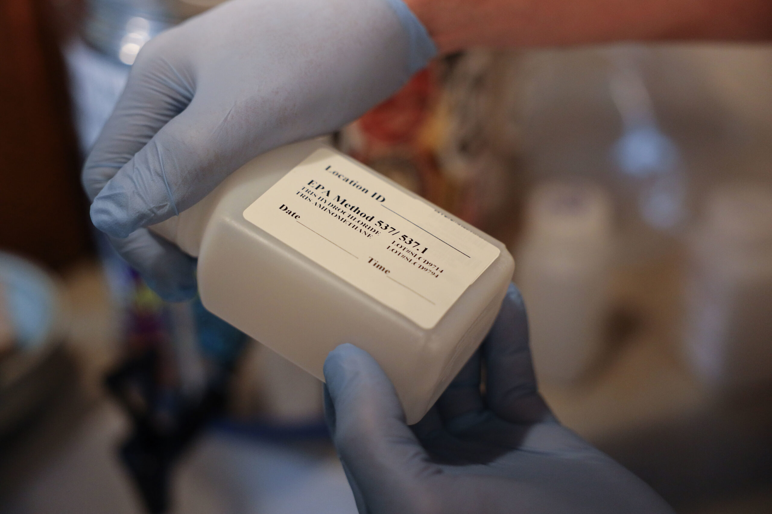 A person wearing gloves is hodling a bottle that will contain water to be tested for PFAS.