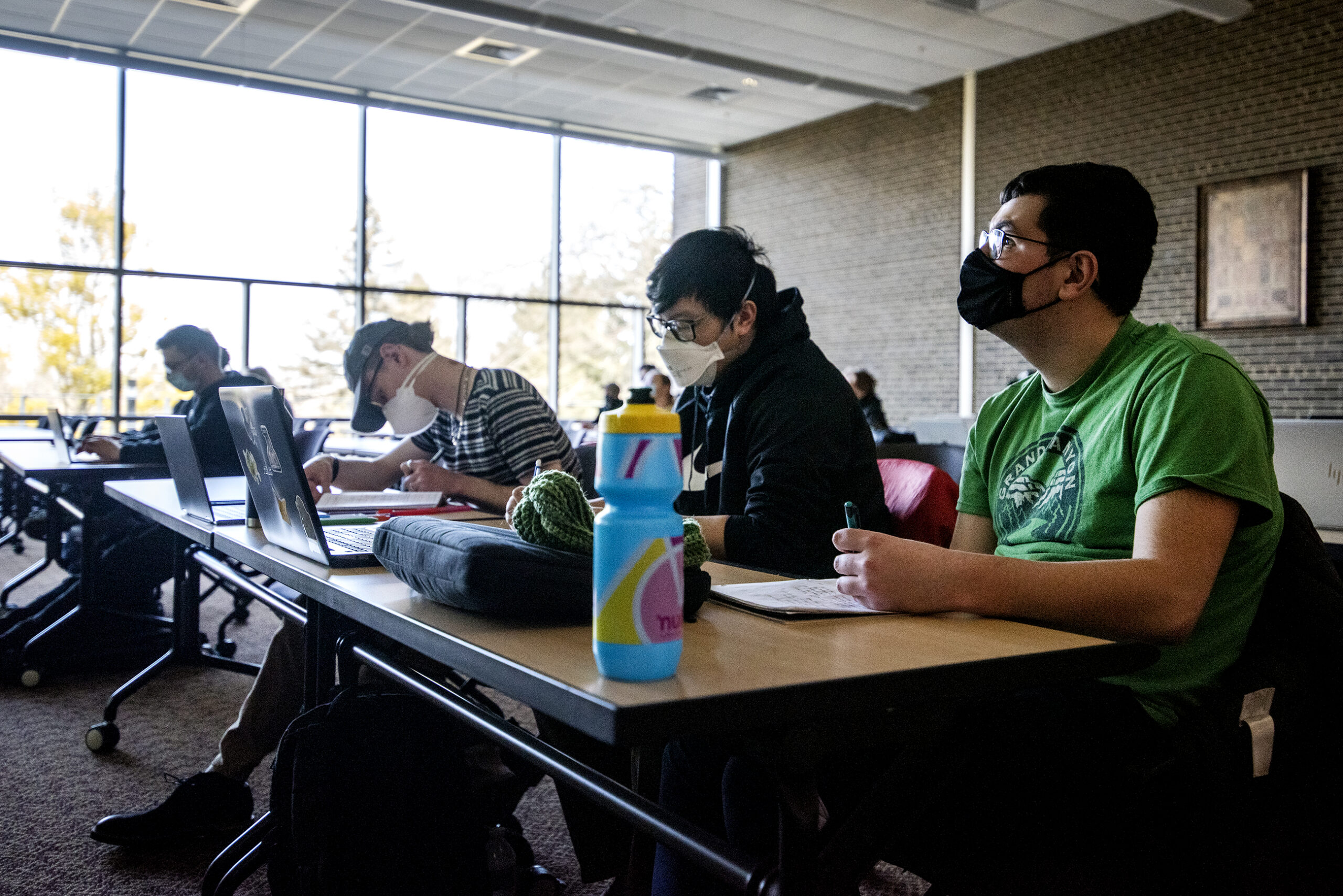 Three students sit next to each other in a class during a lecture.