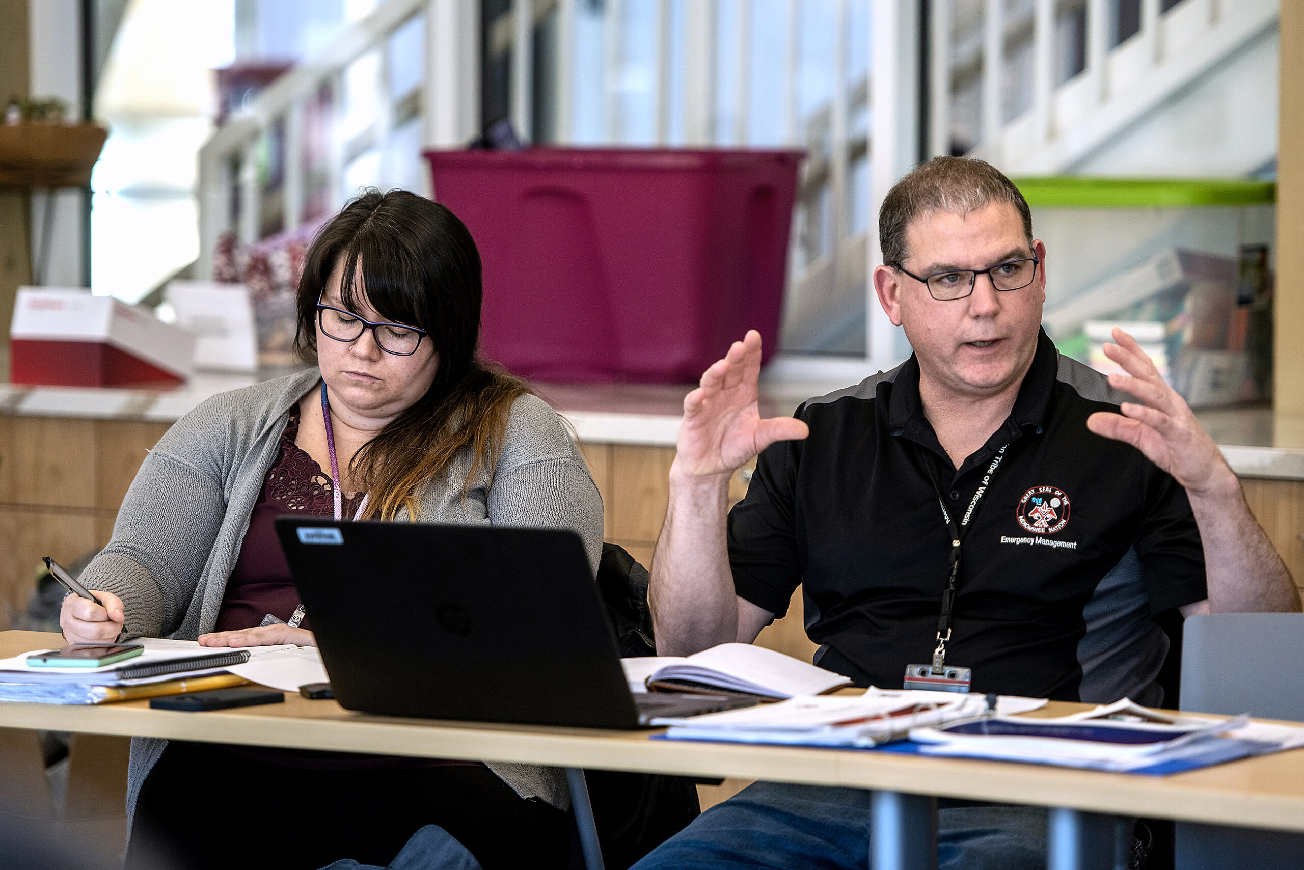 Two people at a table lead a meeting. A man gestures with his hands while speaking.