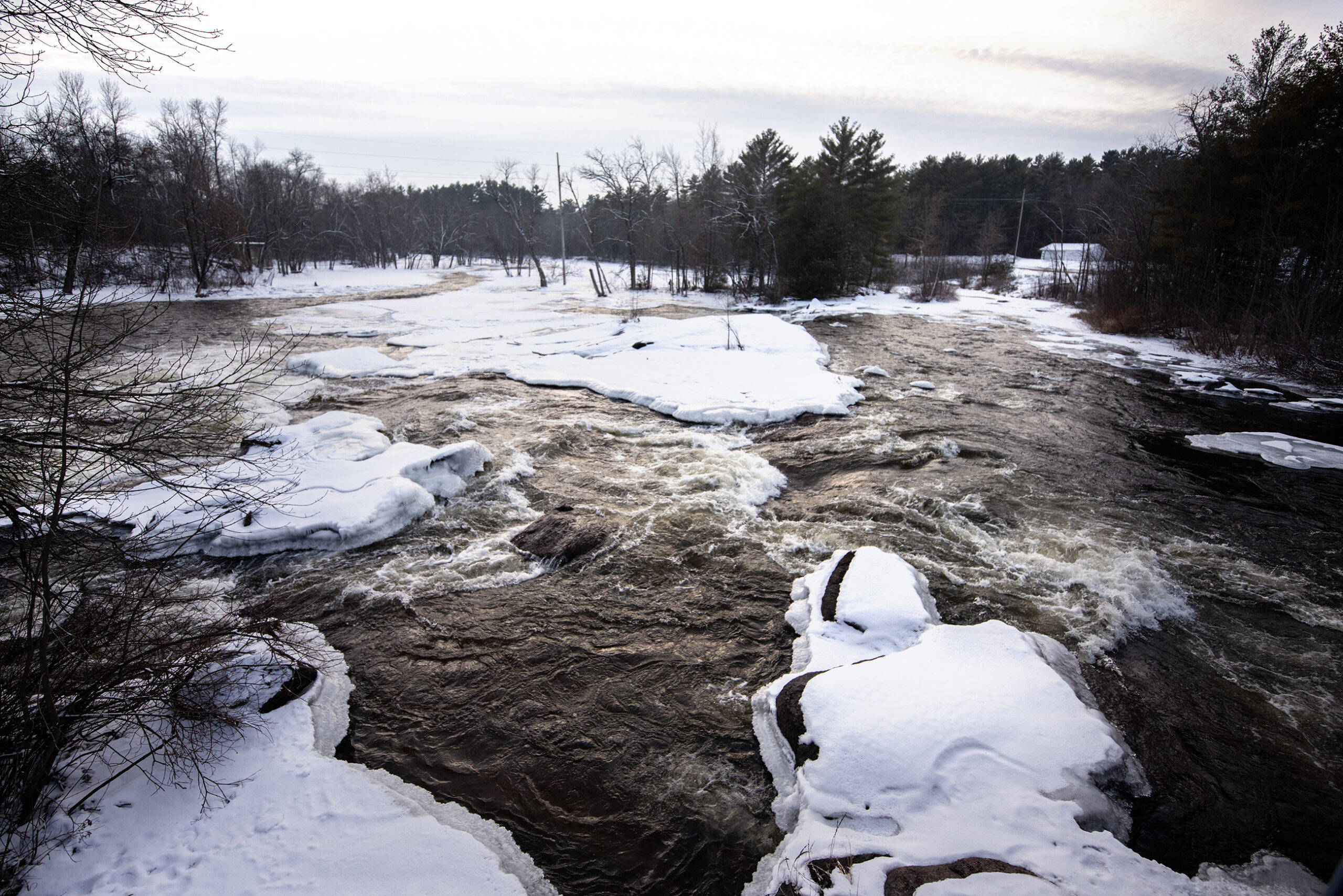 Water forms white waves as it rushes around snow, ice, and rocks.