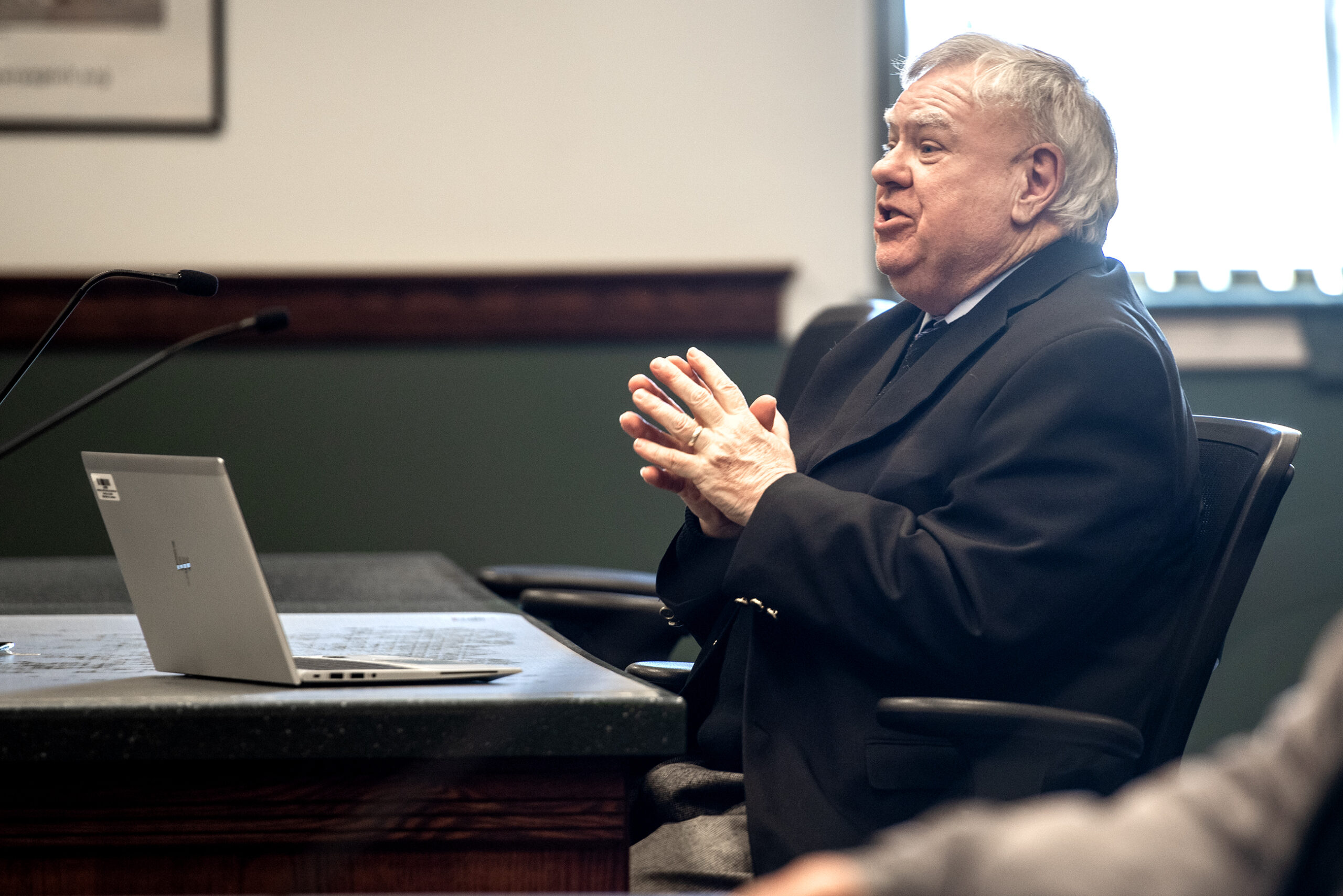 A man sits in a chair at a table in a courtroom.