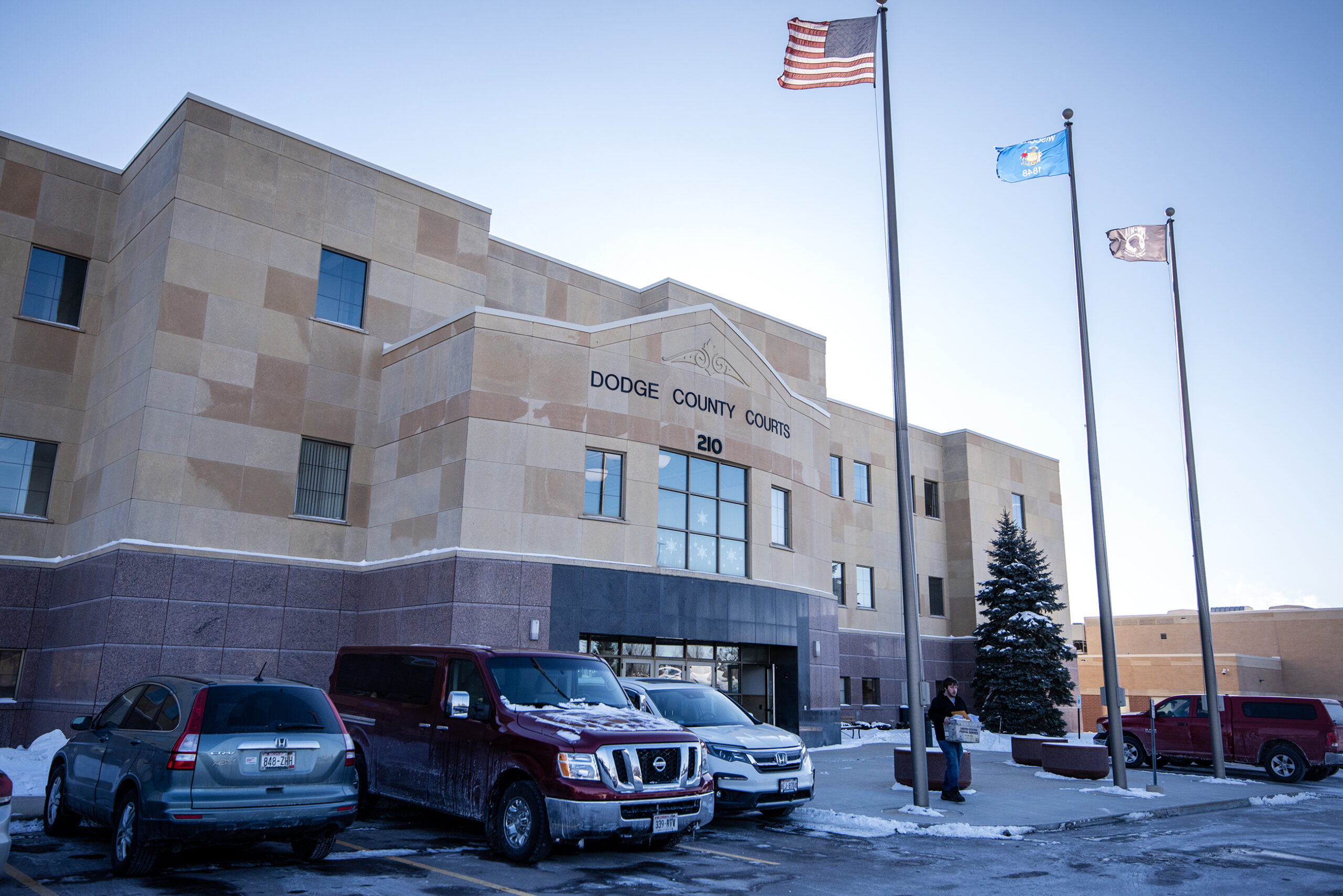 Three flags fly above a tan building that says 