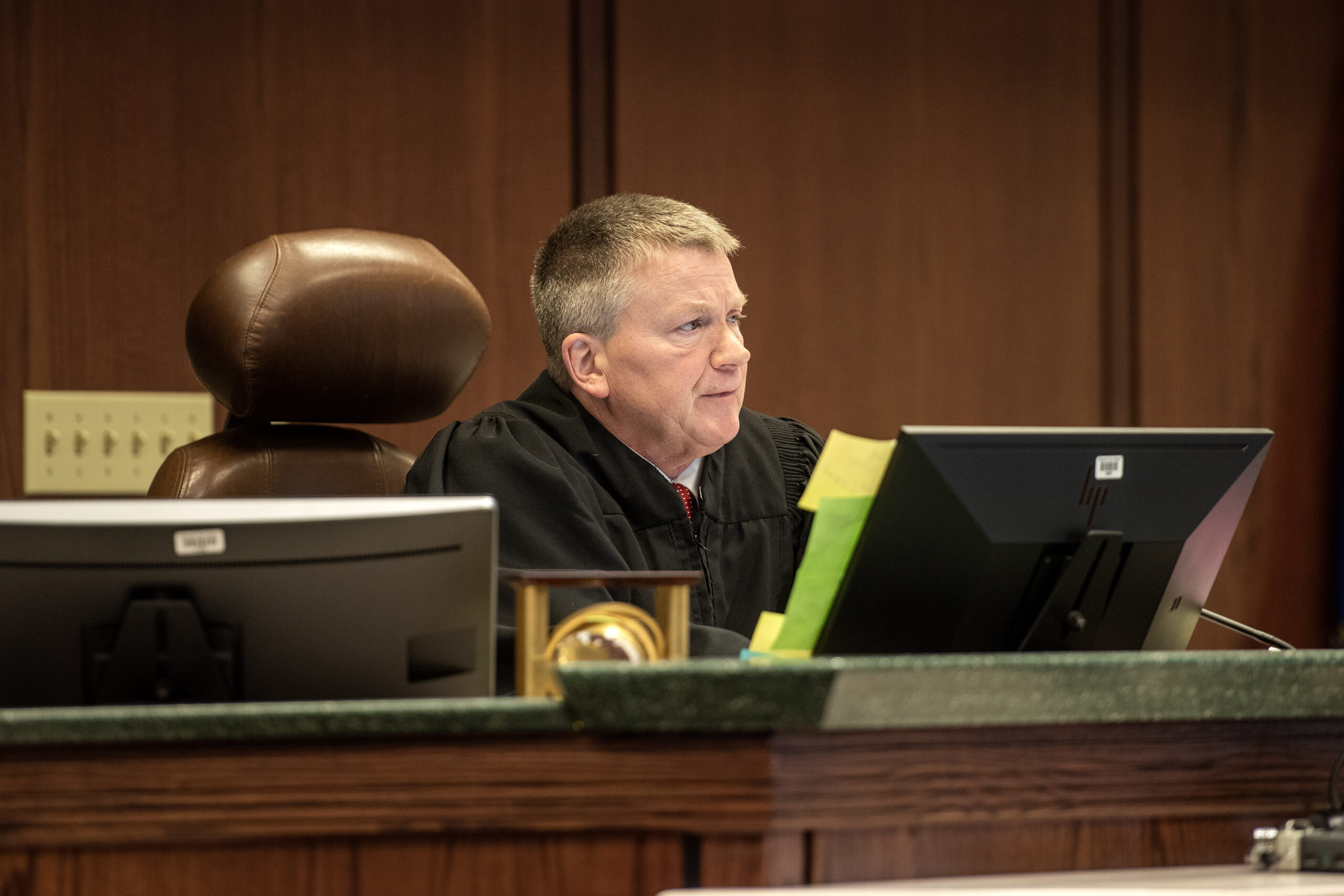 A judge sits at the front of the courtroom in a black robe.