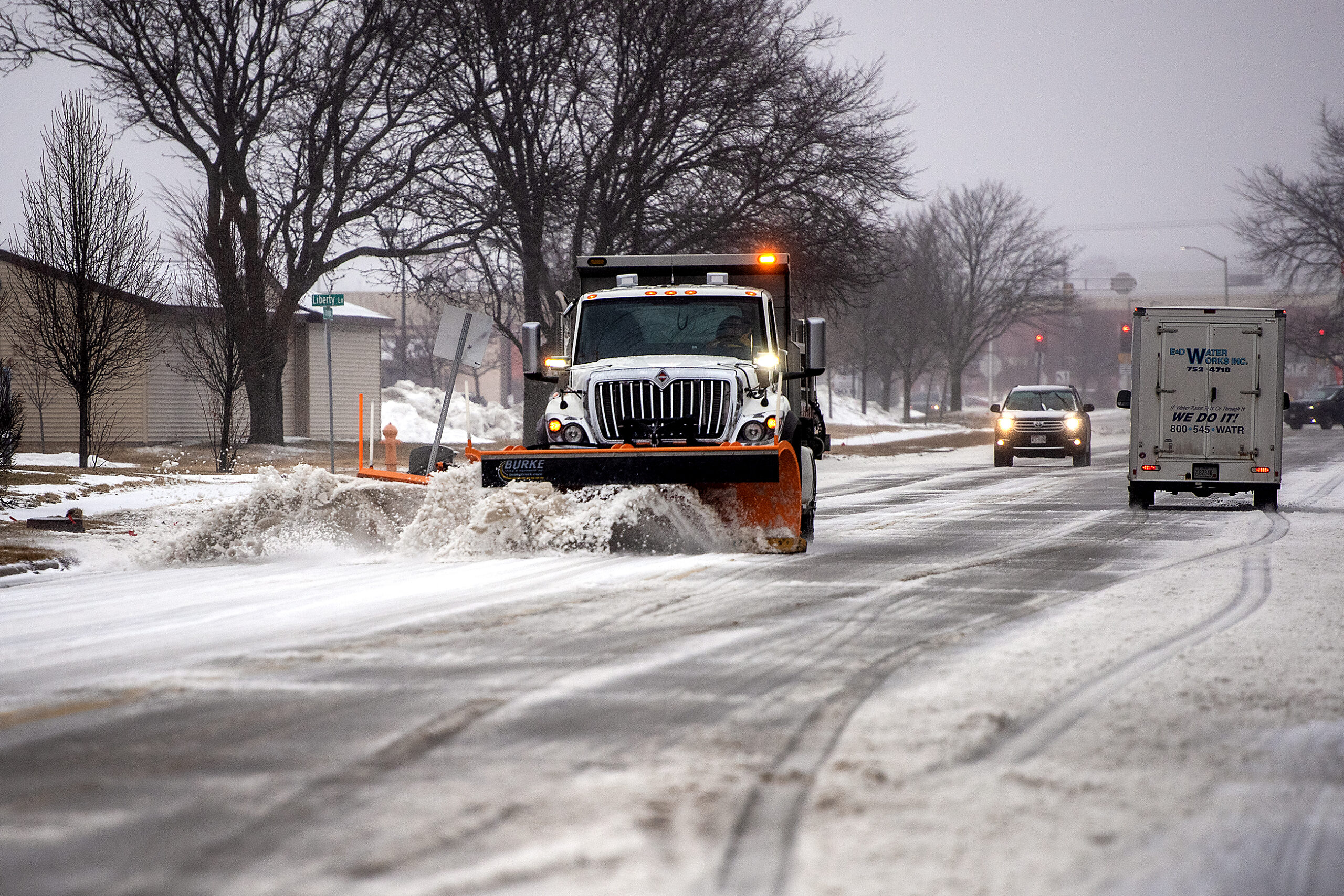 Snow sloshes as it is moved to the side of the street by a white truck with an orange plow.