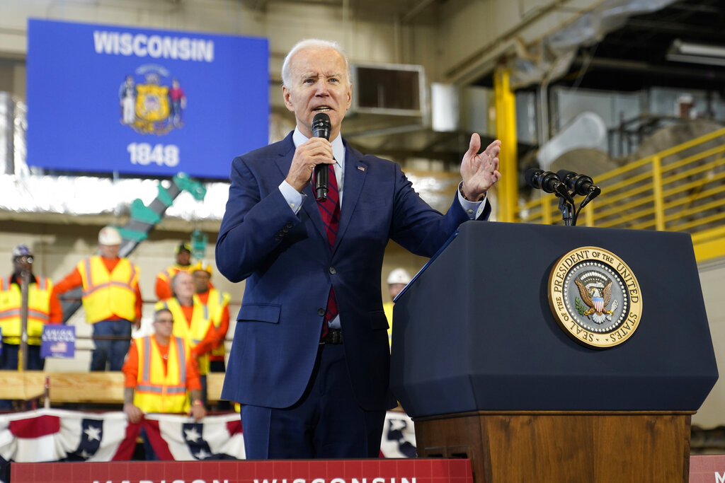 President Joe Biden speaks in front of workers and a state of Wisconsin flag