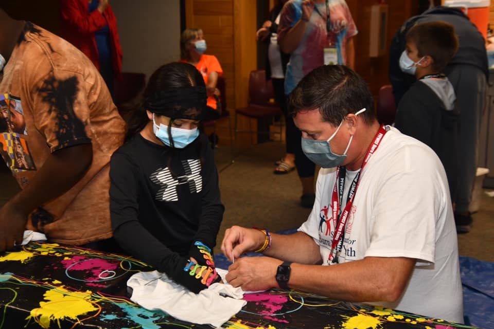 A camp counselor helps a camper during a tie dye activity