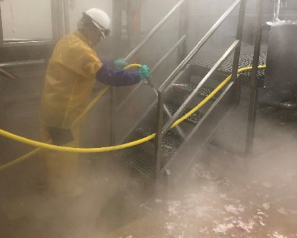 An employee in a yellow suit washes down a staircase with a hose in a hazy room