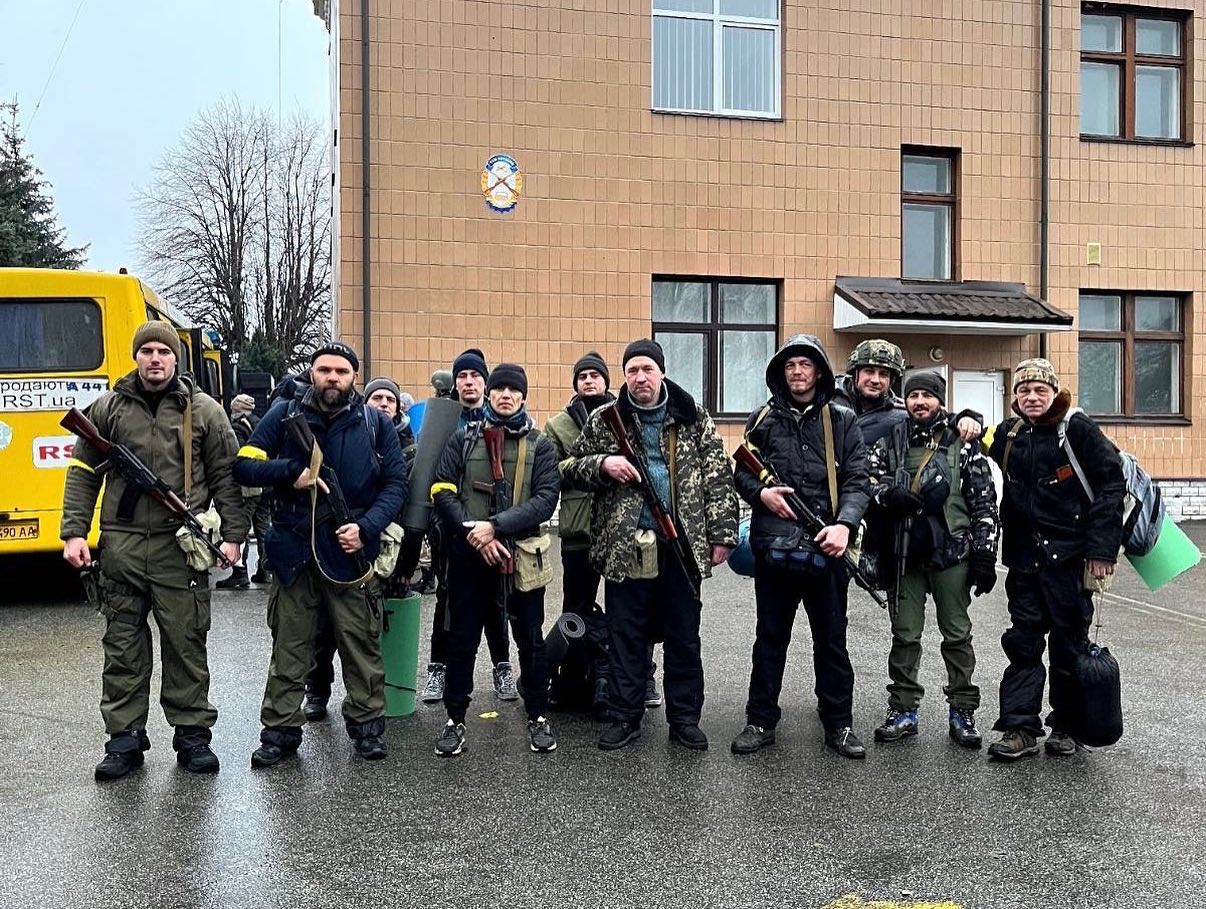 Valentyn Potapenko stands with a group of others, some dressed in camouflaged jackets and holding guns