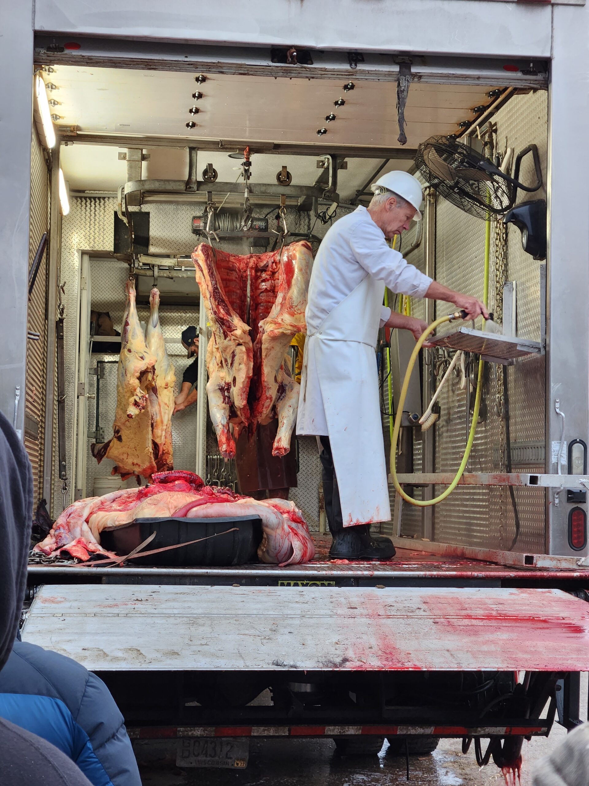 A man stands in the back of a track butchering meat