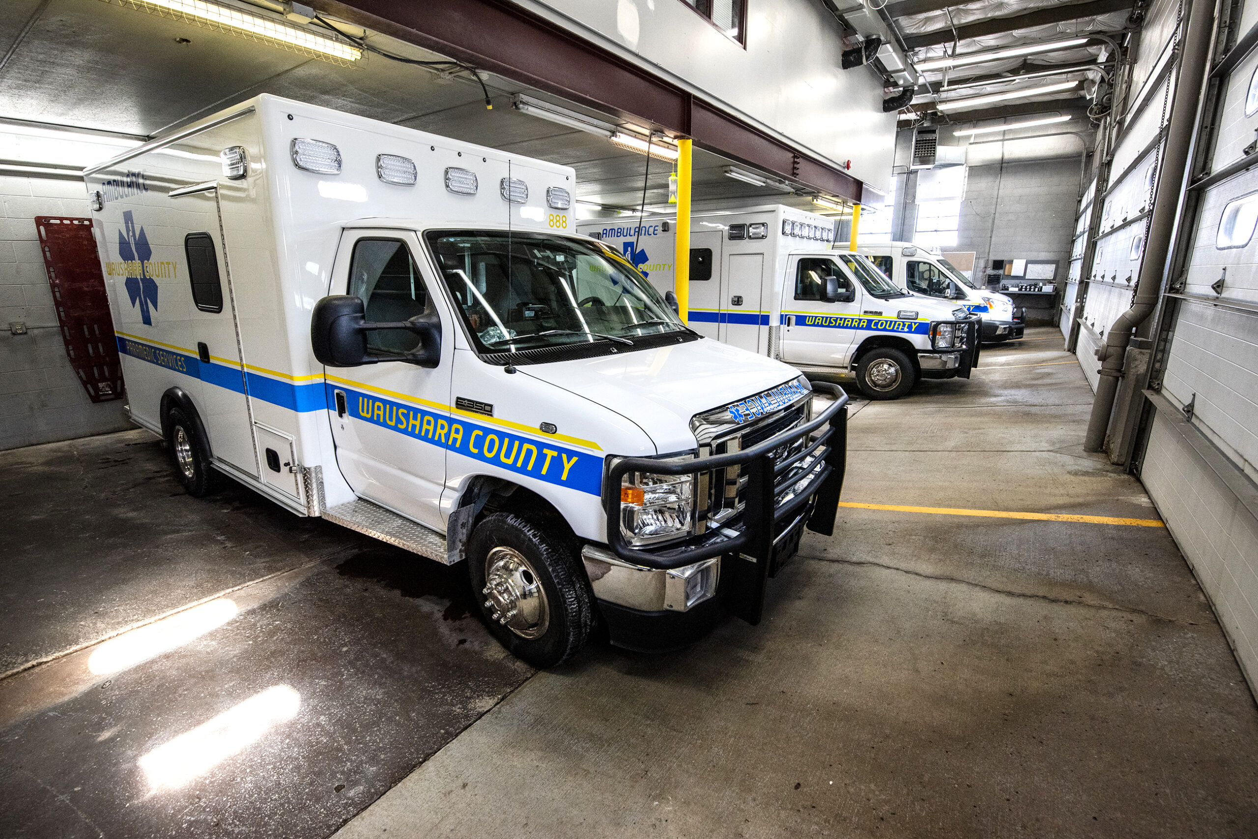 Three ambulances are parked in a garage with closed doors.