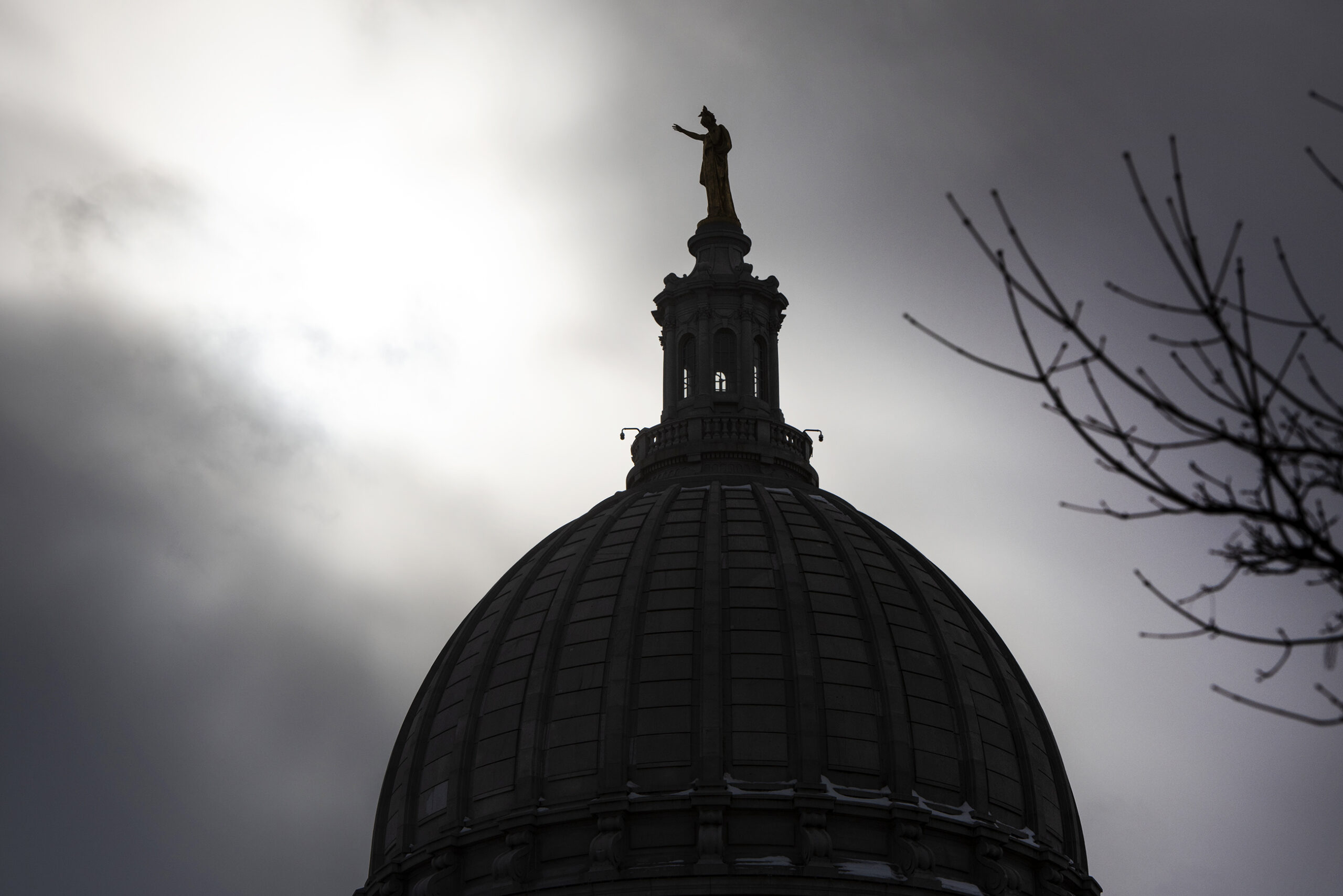 A silhouetted "Wisconsin" statue is seen in front of dark clouds.