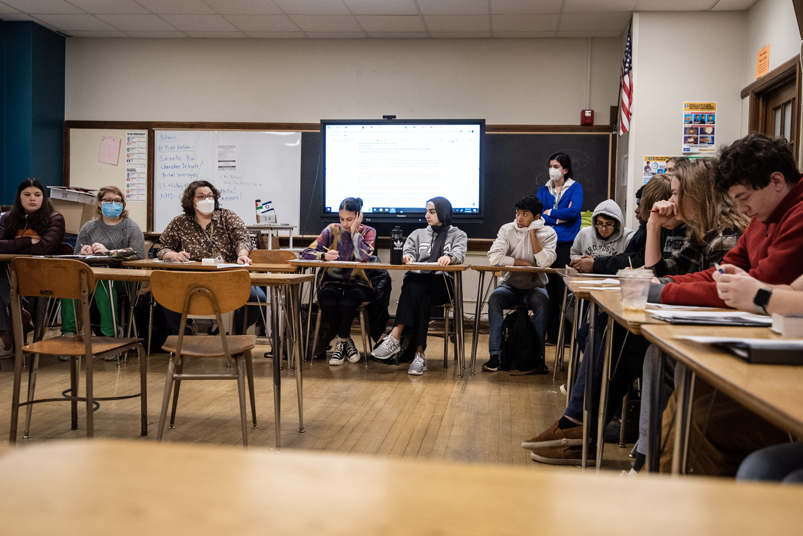 A line of students sit in desks in a classroom.