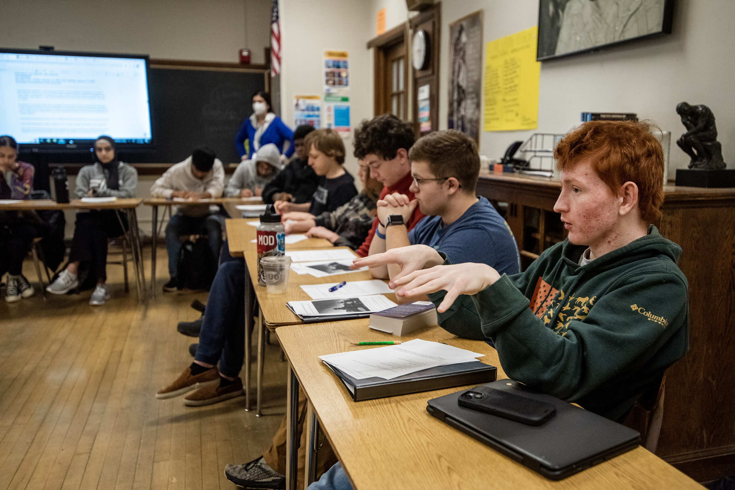 A student gestures as he addresses his fellow classmates in a classroom.