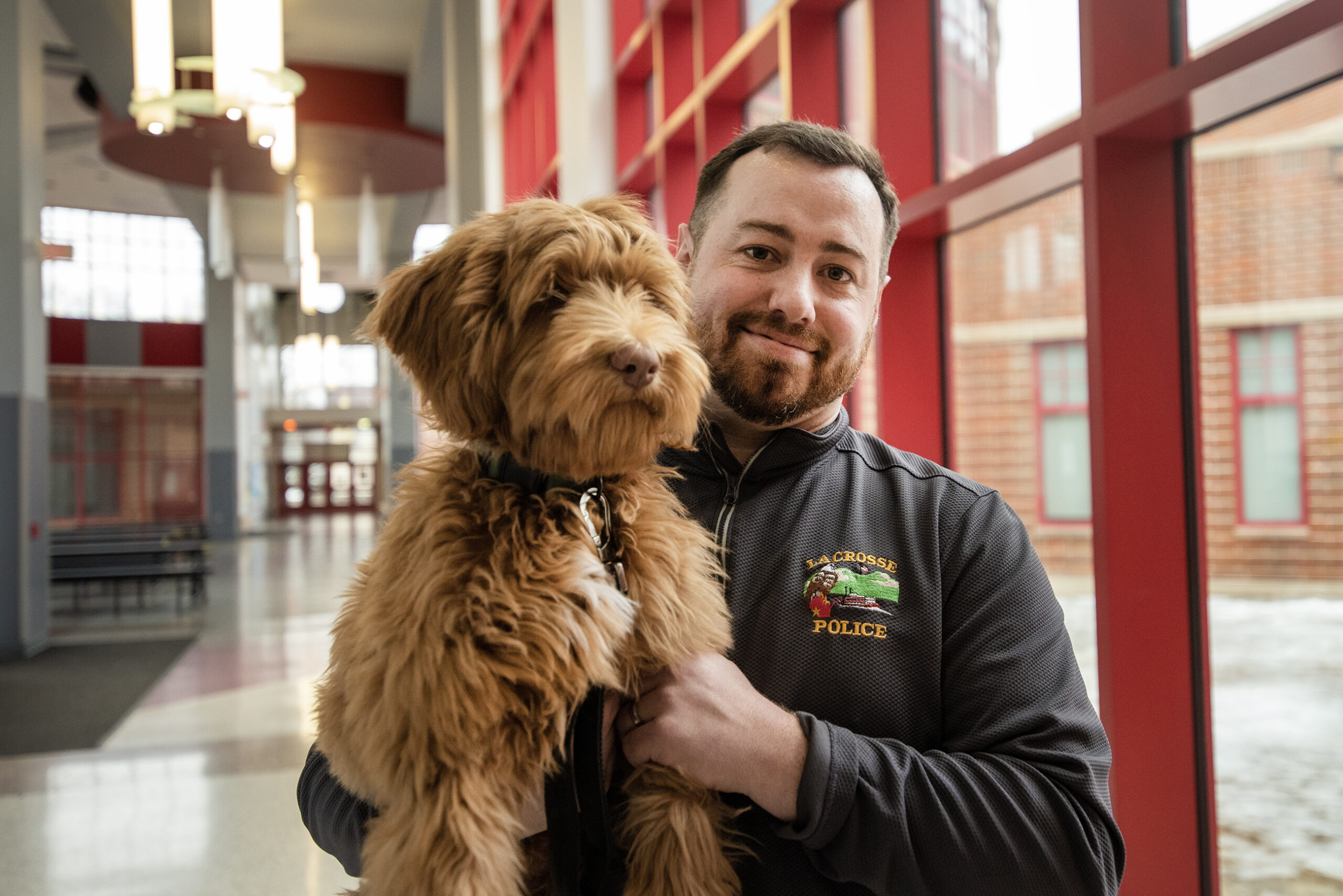 An officer holds a brown fluffy dog in a school.