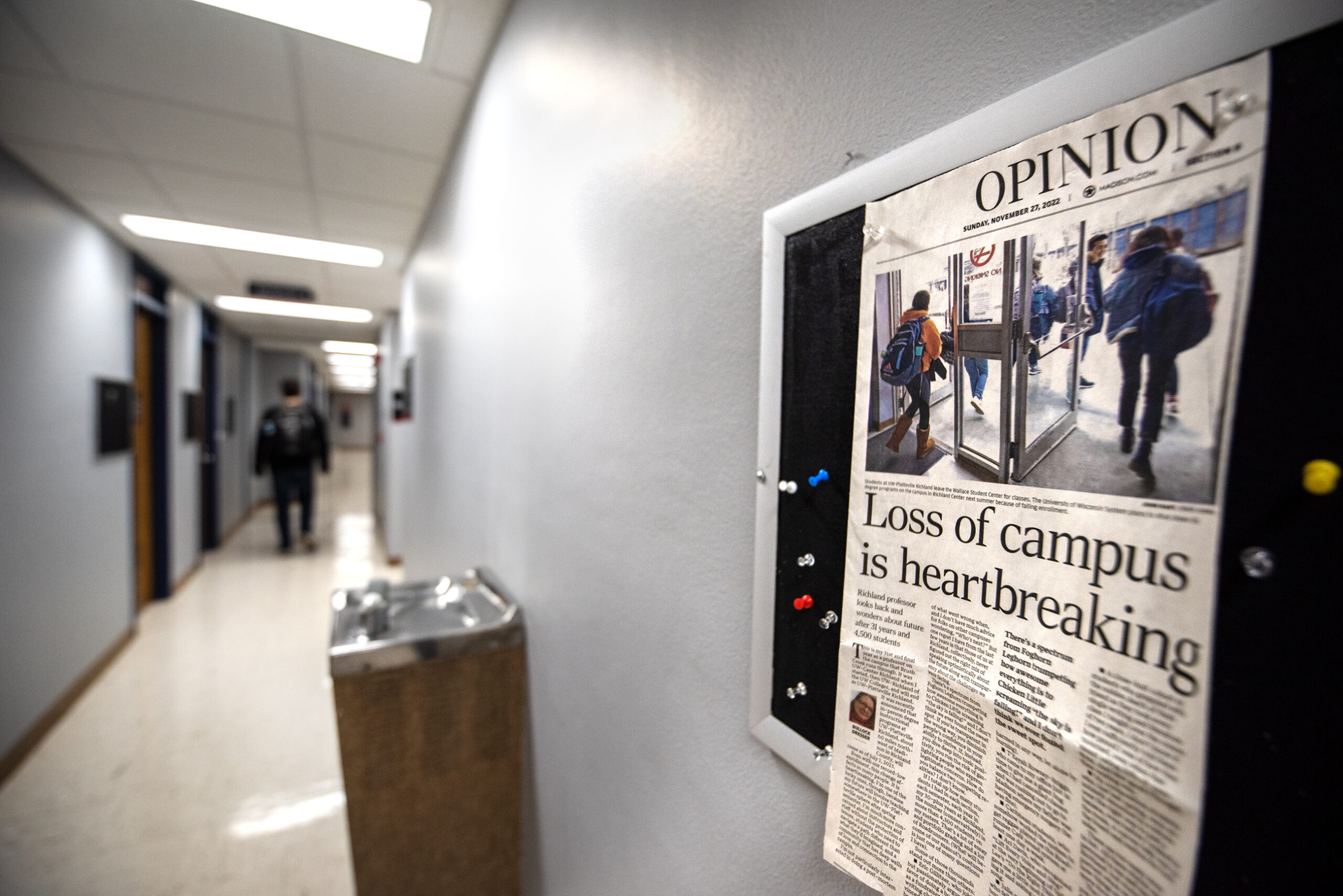 A newspaper is pinned to a bulletin board in a hallway. A headline says "Loss of campus is heartbreaking."