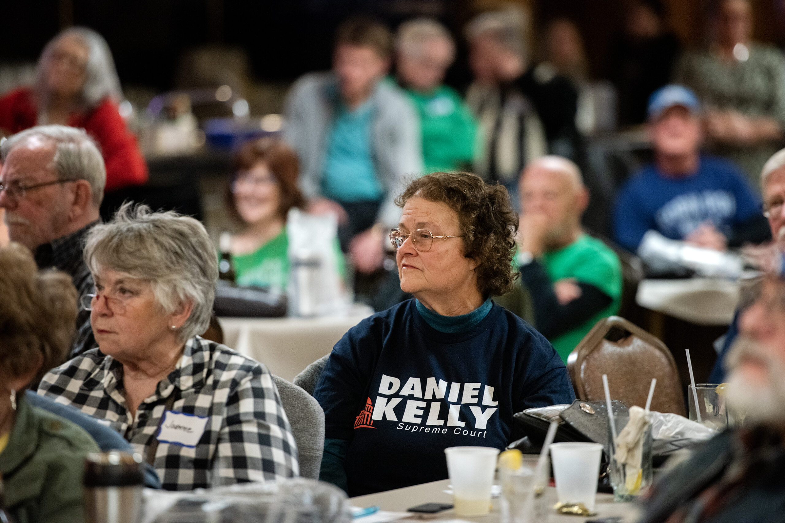 A woman wears a shirt with Dan Kelly's name on it while sitting in a supper club.