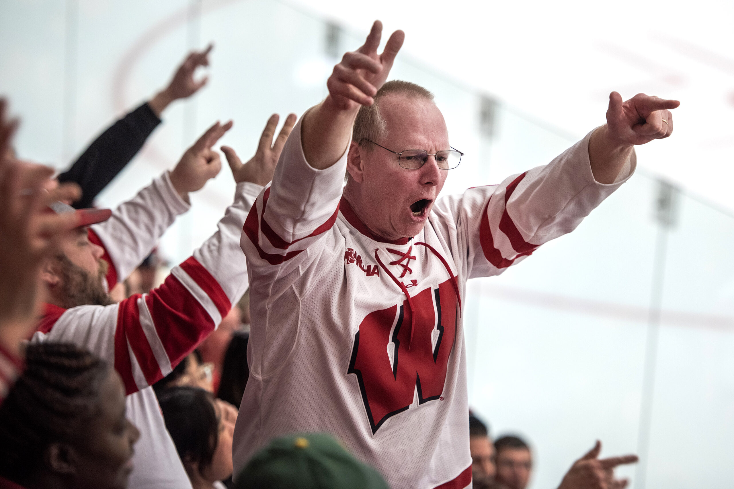 A fan in a Badgers jersey holds up seven fingers as he chants with the crowd.