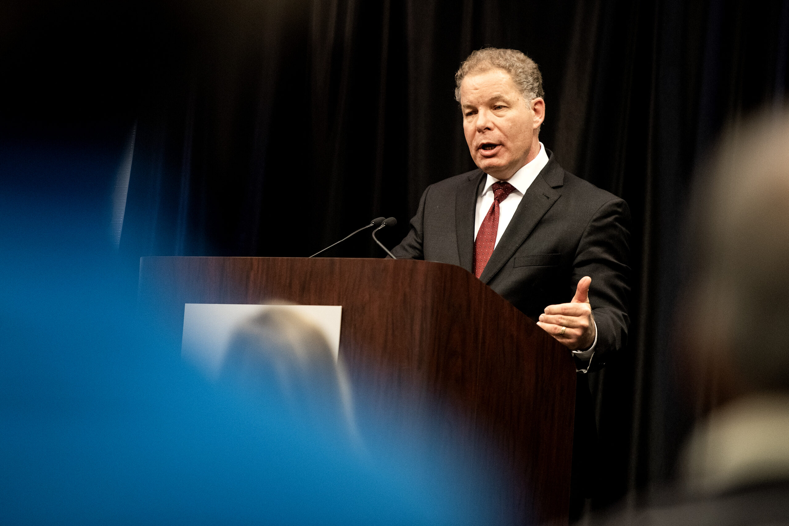 Dan Kelly speaks at a podium as people watch from the crowd.