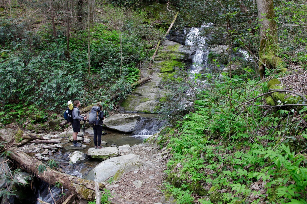 Hikers stand at the base of a waterfall off a hiking trail.