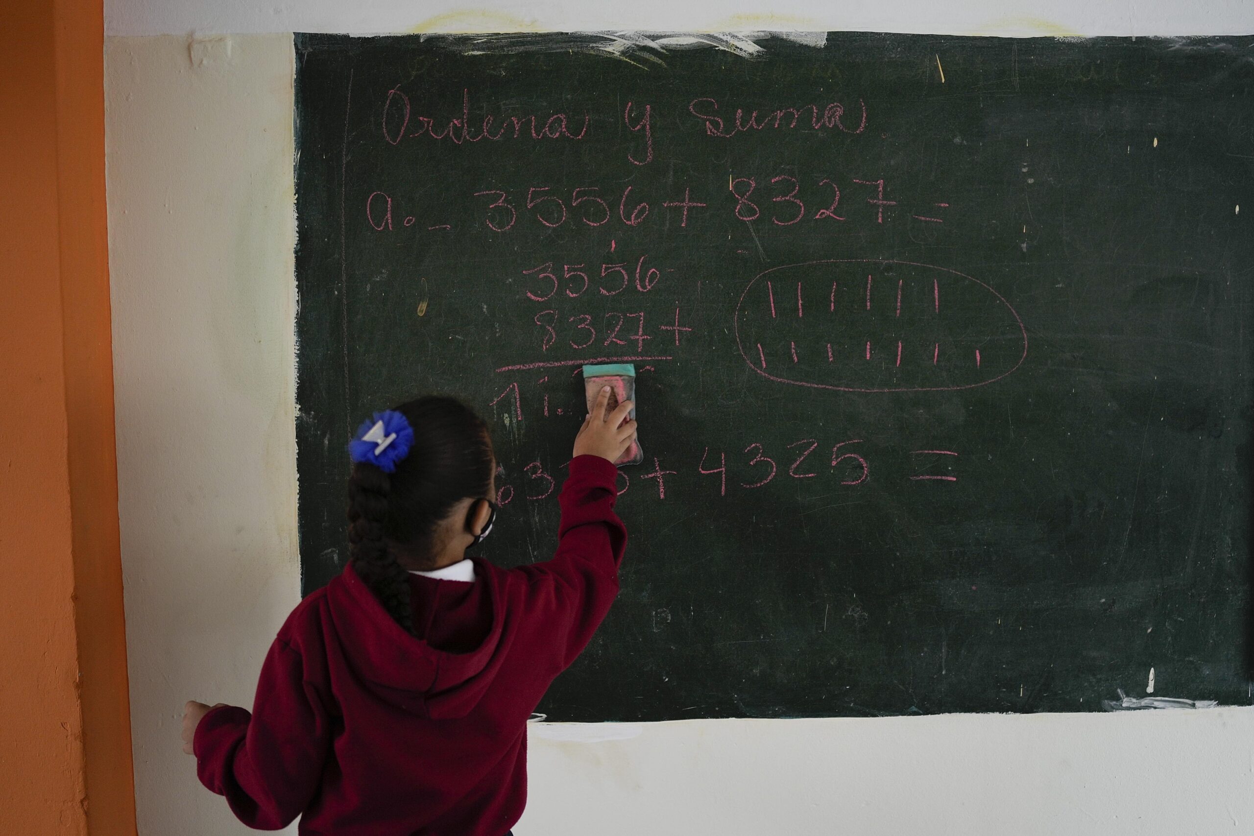A little girl erases a math problem from the chalkboard.