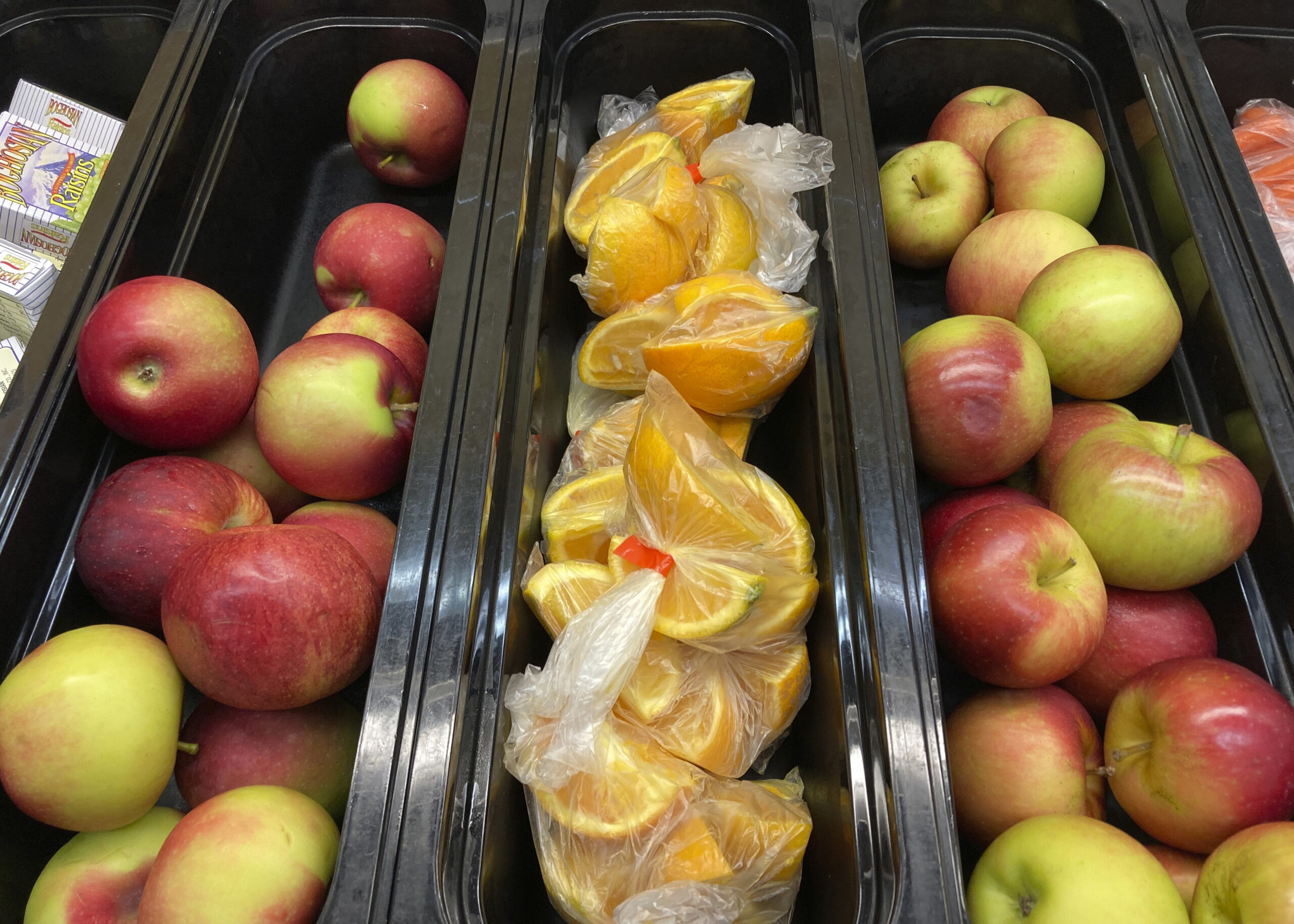 Apples and orange slices rest in trays for student lunch.