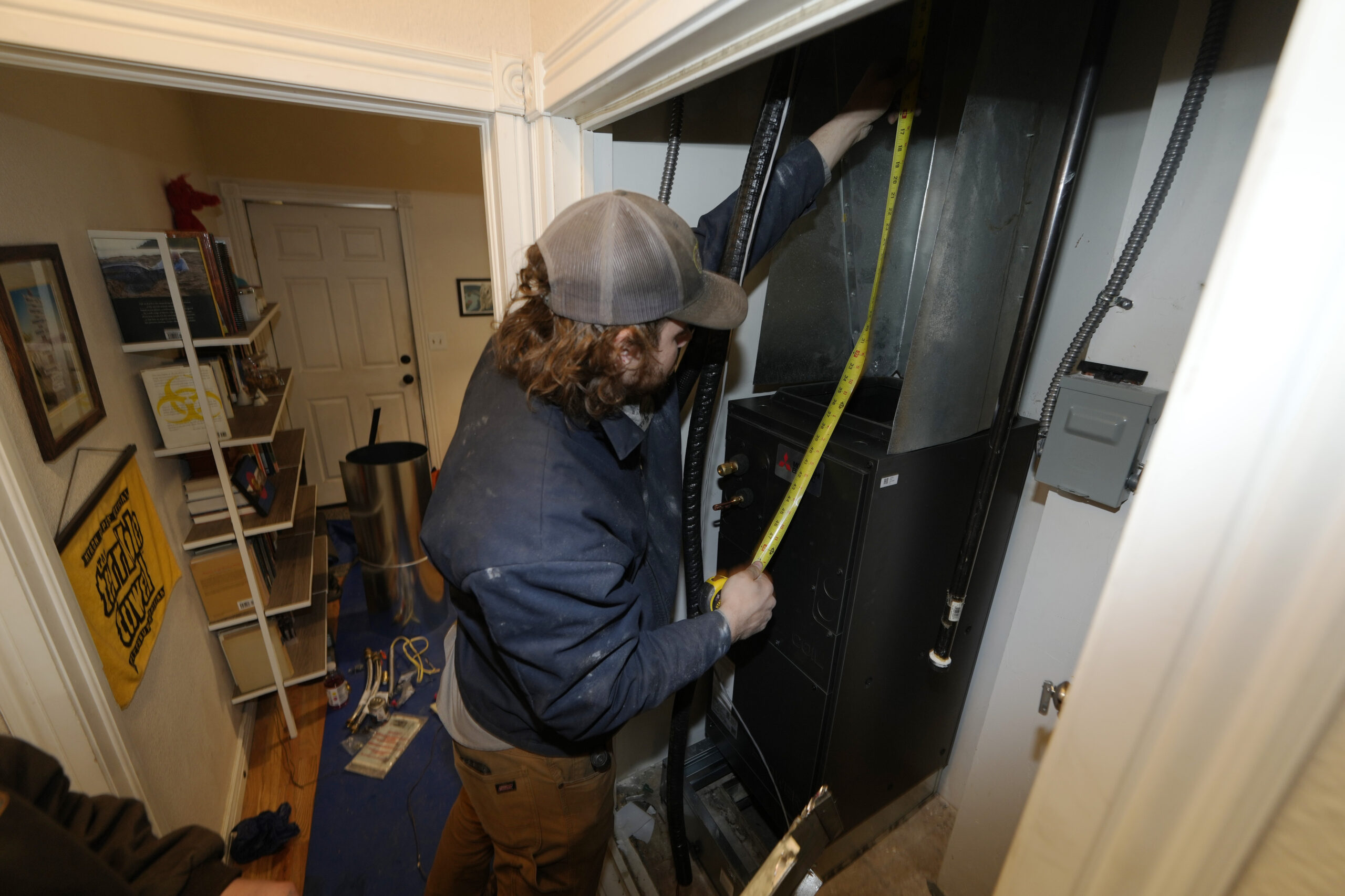 A man uses a tape measure while installing a heat pump