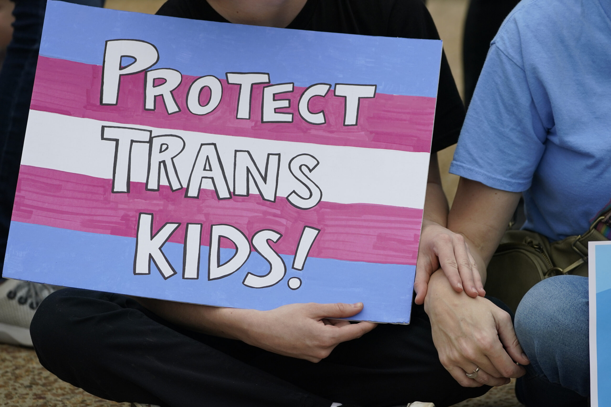 protester holds a poster calling for lawmakers to protect trans children