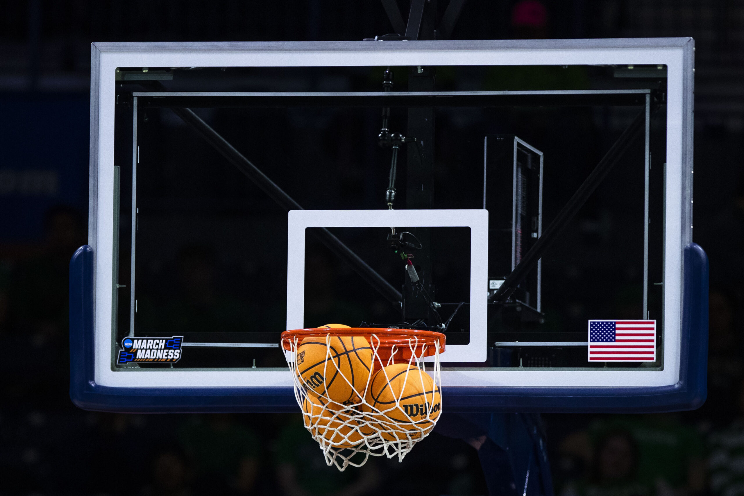 Three basketballs are stuck in the net of a basketball hoop with a glass backboard.