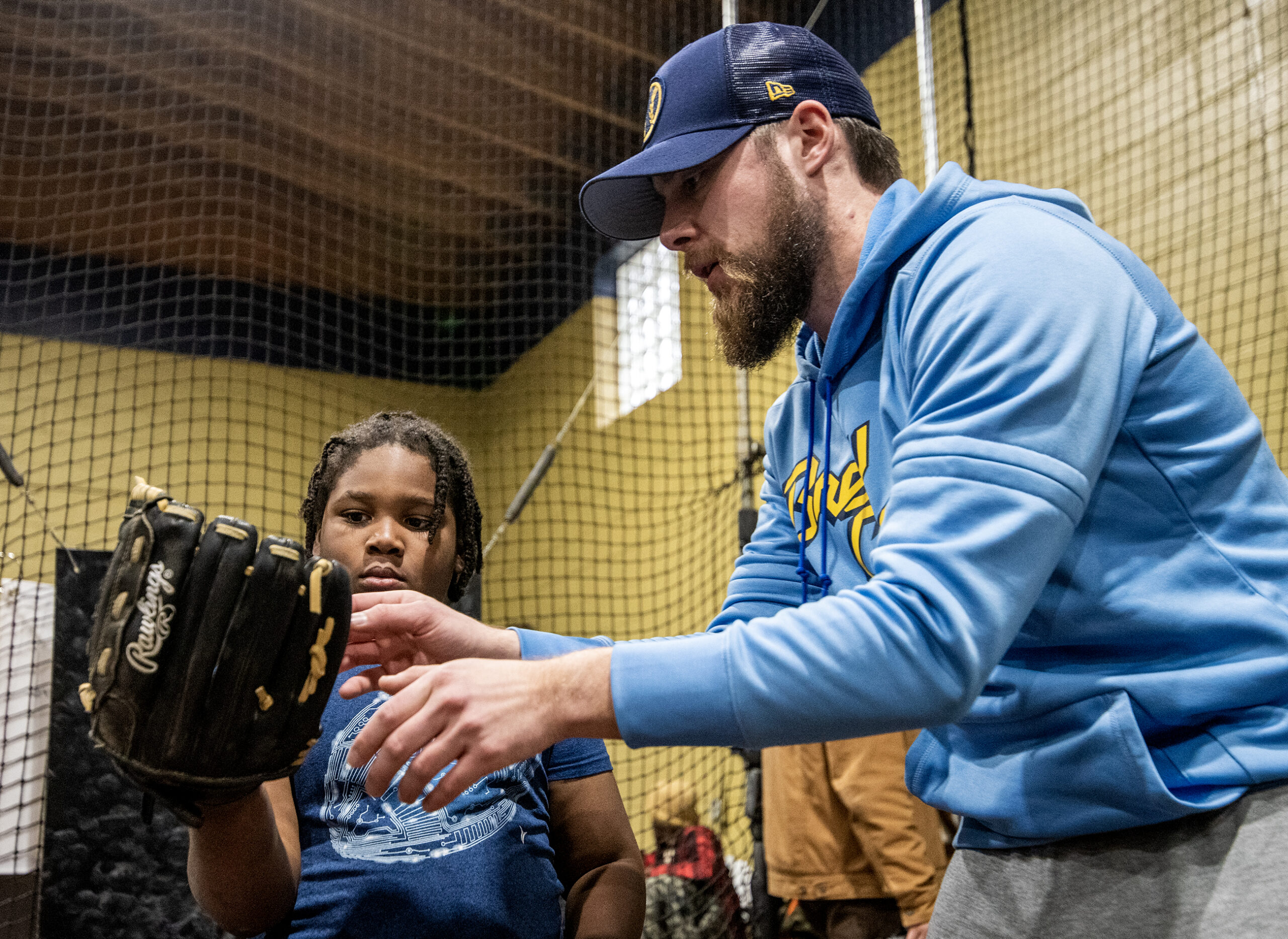 A child looks at their hand in a glove while a coach helps.