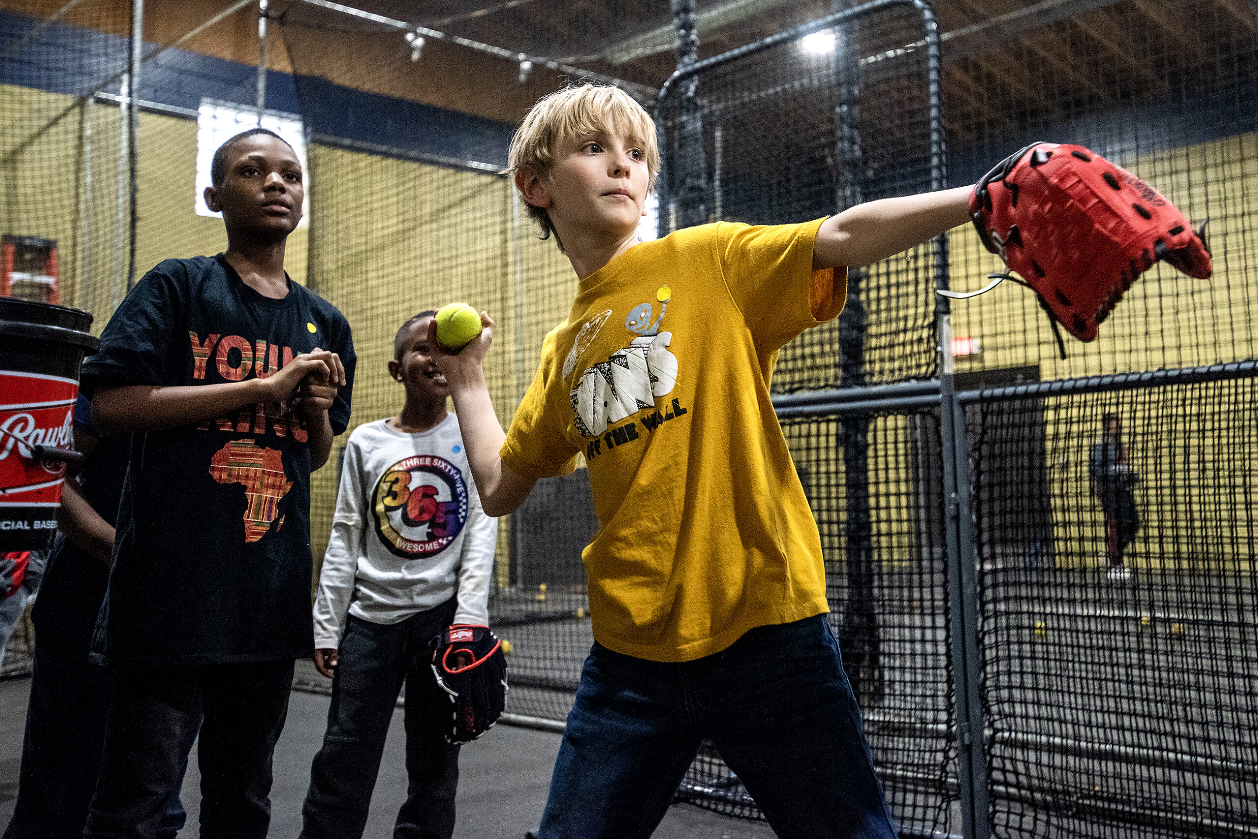 A child in a yellow shirt throws a ball in an indoor practice facility.
