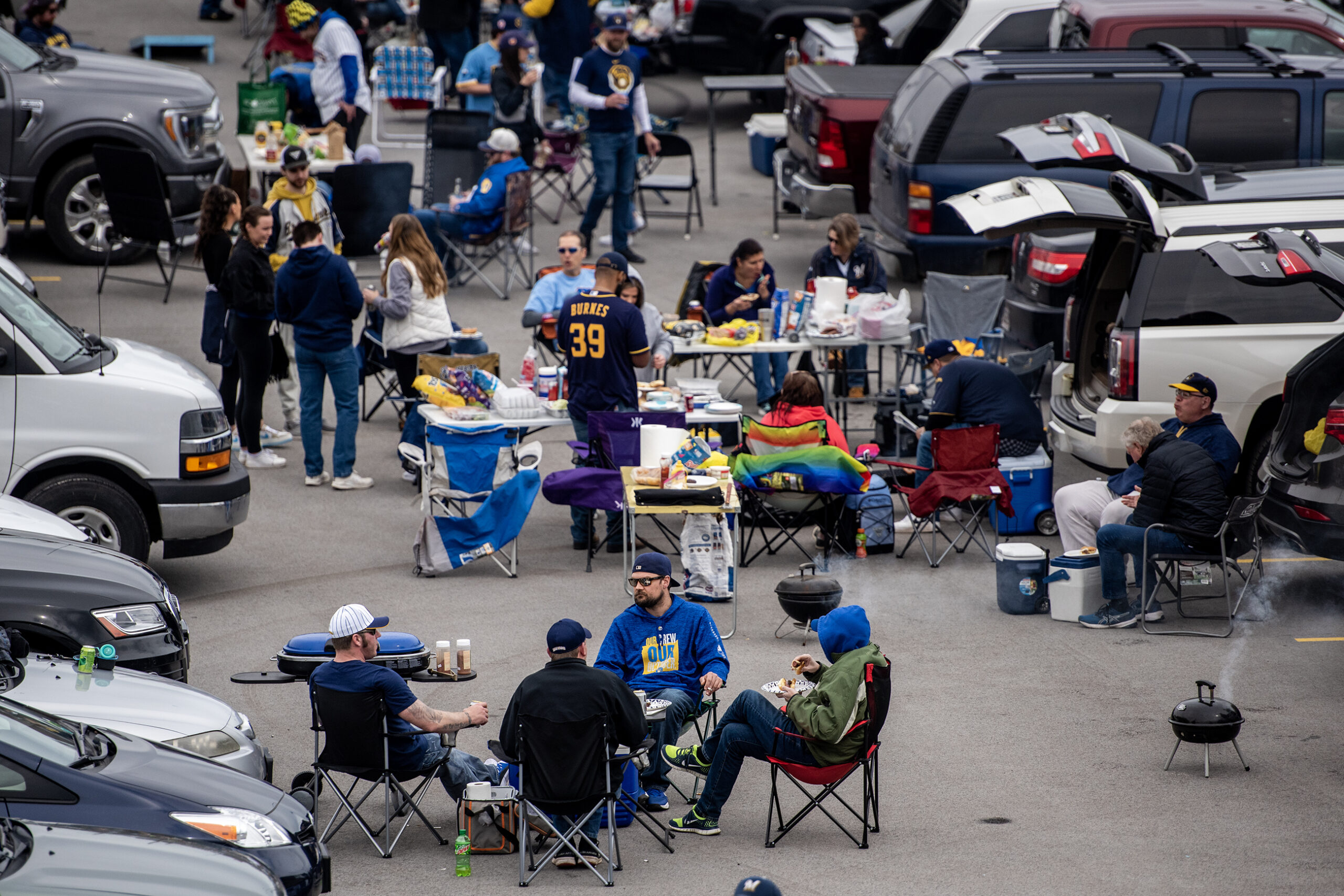 Groups of people in lawn chairs grill and drink beer in the parking lot.