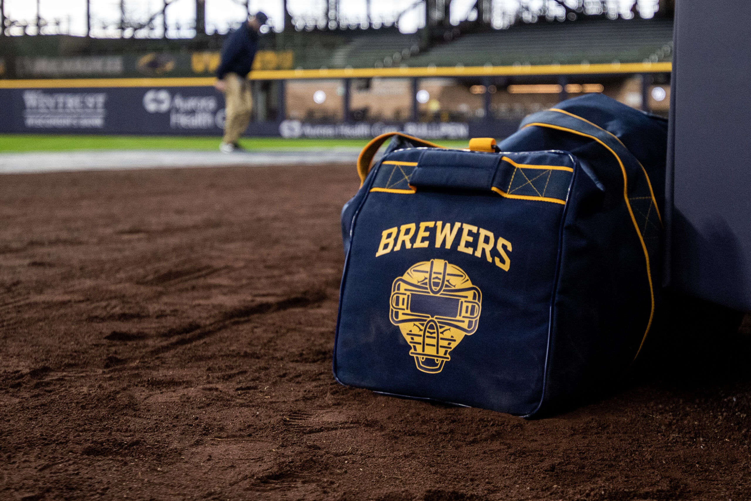 A blue duffel bag sits on dirt. A yellow Brewers logo is seen on the side.