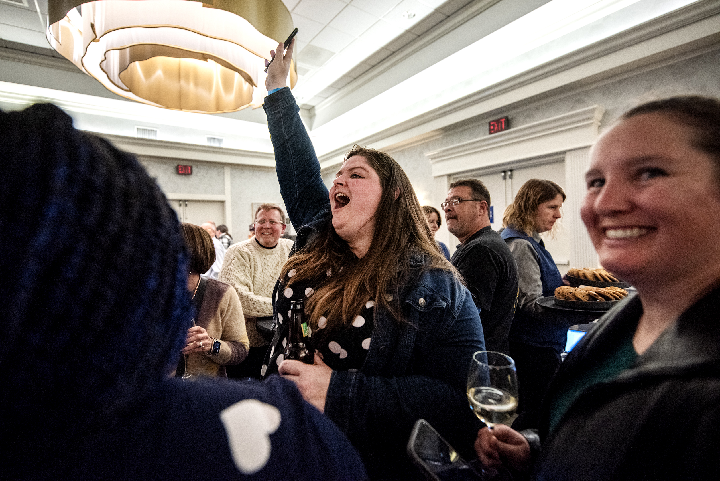 A woman raises her fist in the air as she shouts. People around her smile.