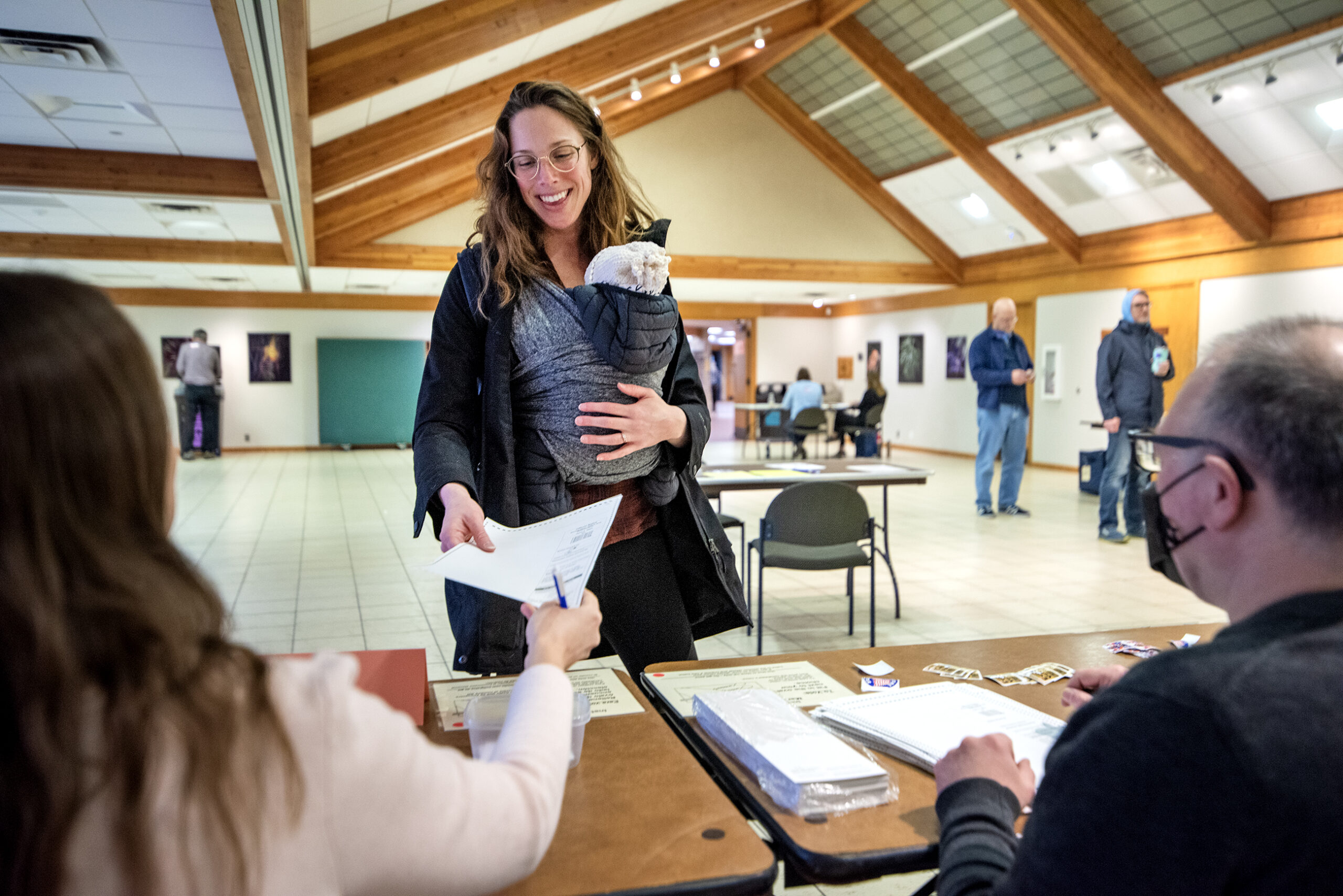 A woman holding a baby smiles as she reaches for a ballot.