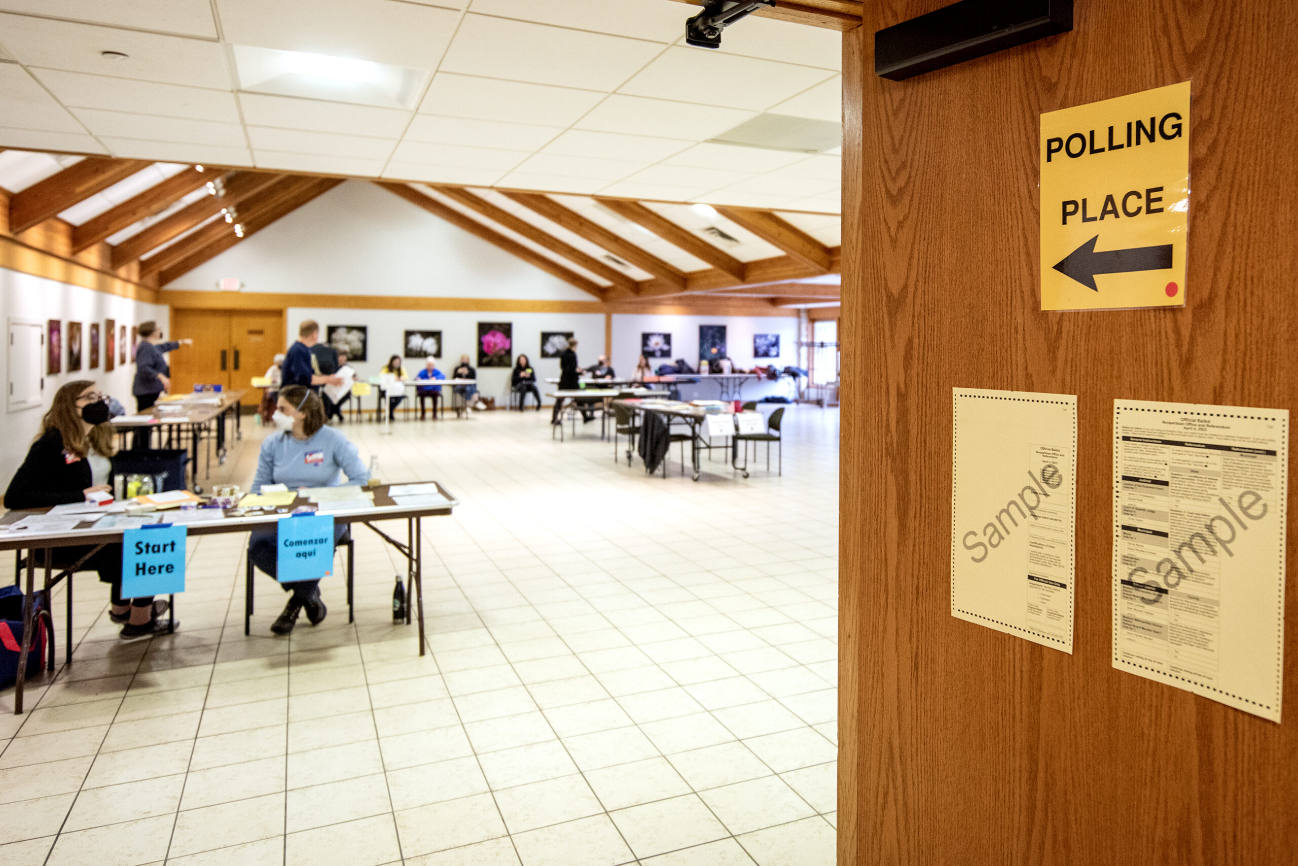 A sign says "Polling Place" with an arrow into a room where workers sit at tables.