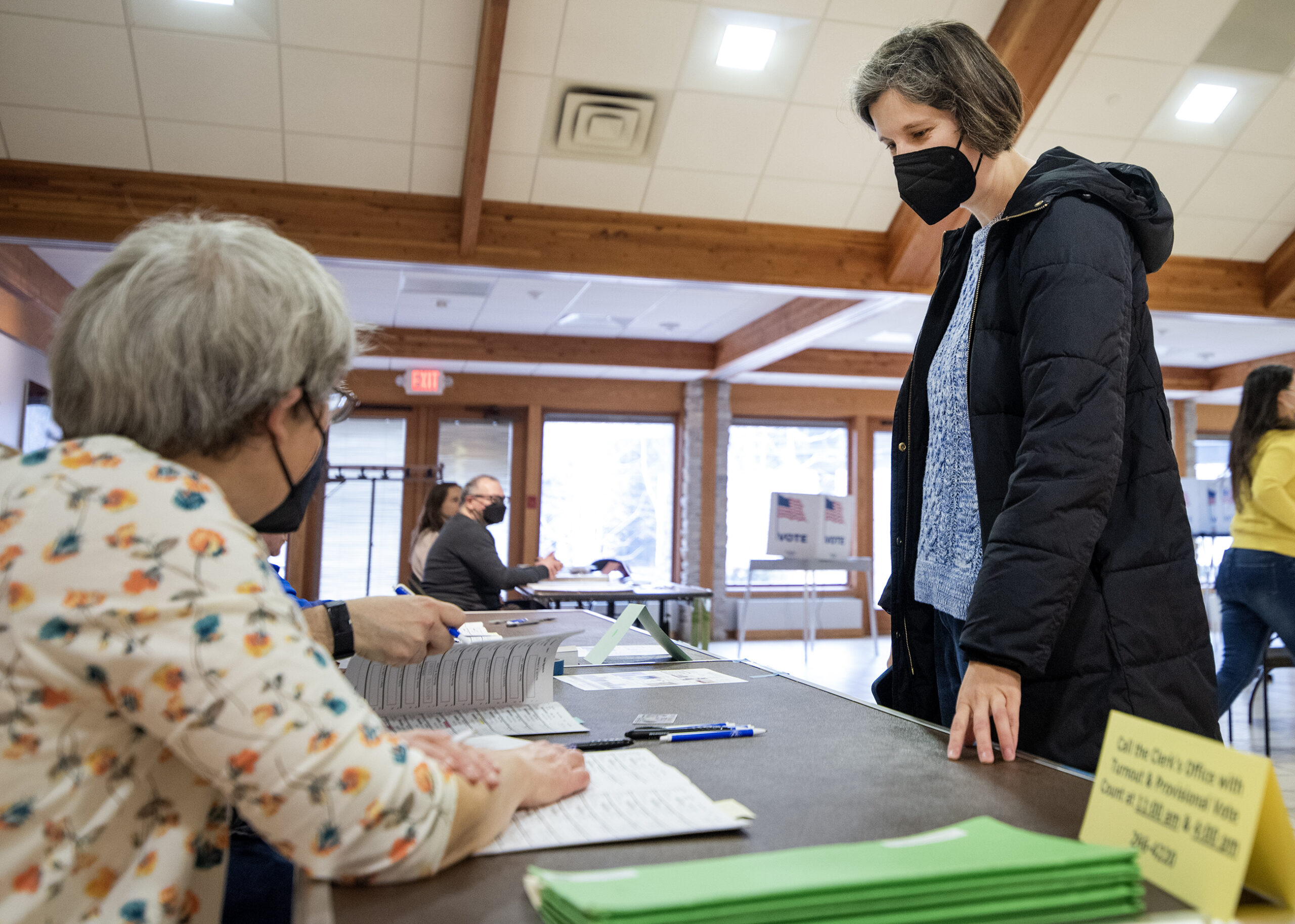 A woman stands at a table as a poll worker finds her name in the book.