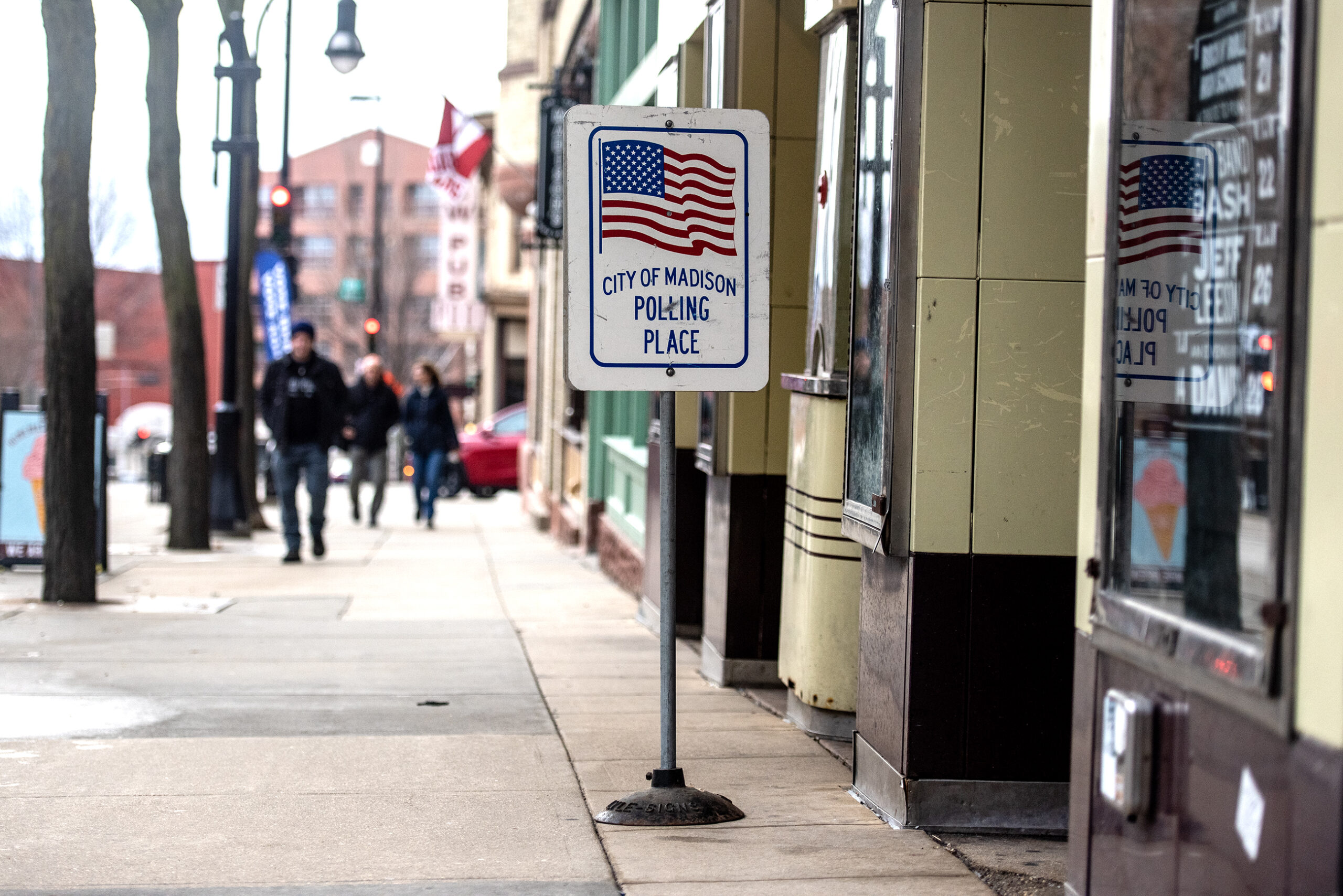 A sign on a sidewalk with a U.S. flag says "City of Madison Polling Place."