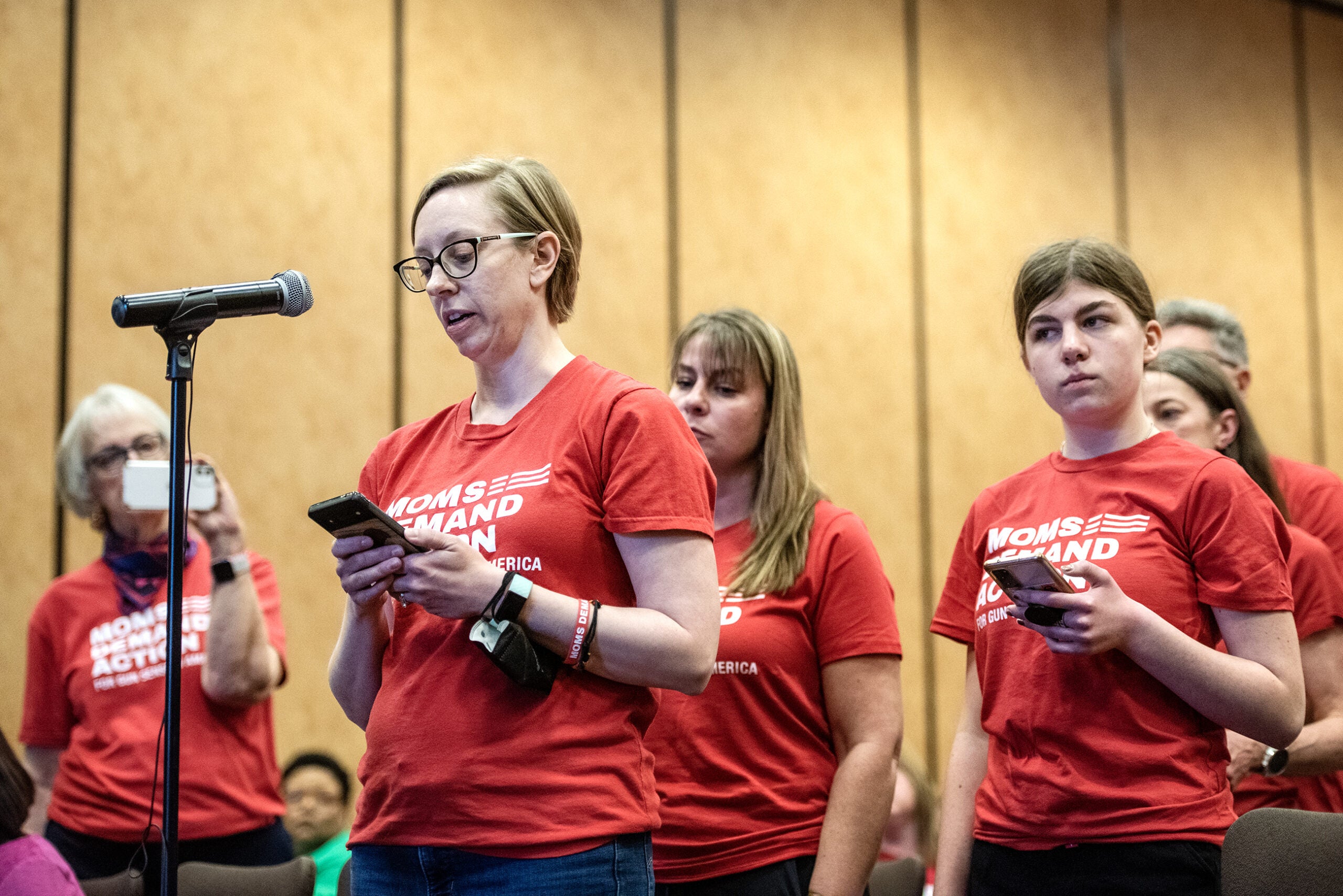 A group stands together in matching red shirts as they confront state legislators.